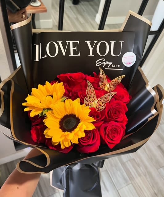 "Bold Love" Bouquet "Bold Love" Bouquet - A daring combination of radiant sunflowers and passionate red roses, wrapped in sleek black with golden accents. For the kind of love that shines bright and speaks boldly.
