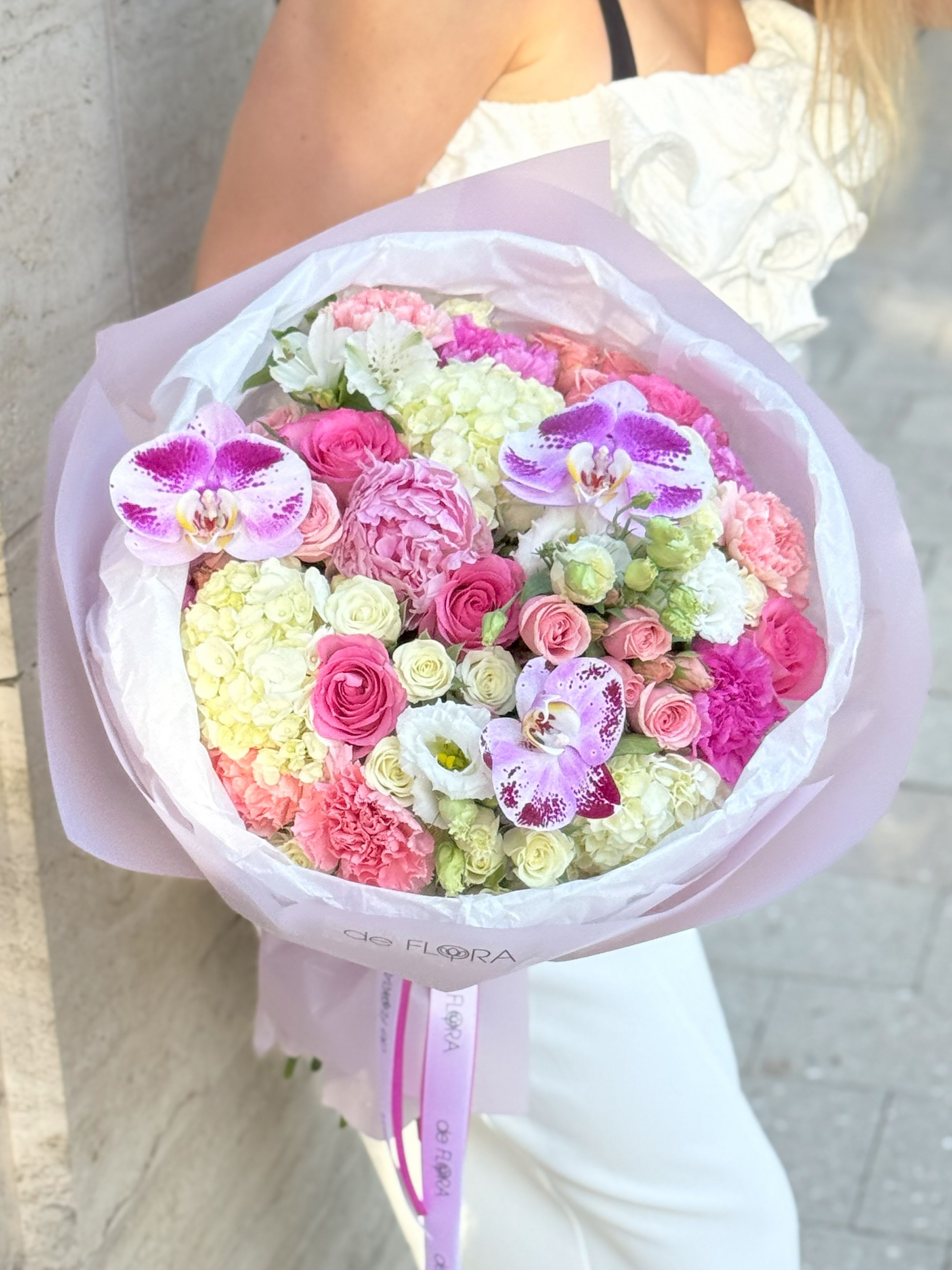 Orchid Kiss - An elegant and radiant bouquet that brings together the finest shades of pink, ivory, and soft green. This lush arrangement features vibrant fuchsia and pastel orchids as the centerpiece, surrounded by delicate roses, lisianthus, carnations, hydrangeas, and spray roses. Wrapped in signature blush paper with branded satin ribbon, Orchid Kiss captures the essence of romance and sophistication — perfect for a special celebration, heartfelt thank-you, or a luxurious “just because” moment.