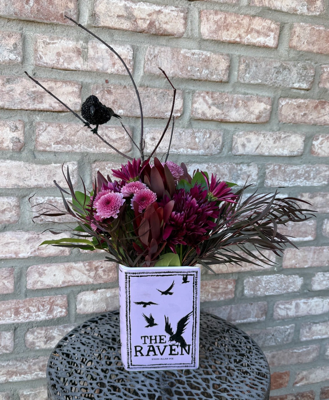 The Raven - Designed in a vase that looks like the book! Filled with long lasting flowers, finished with dark branches and a Raven for aesthetics. Measures approximately 28&quot; tall and 20&quot; wide. 