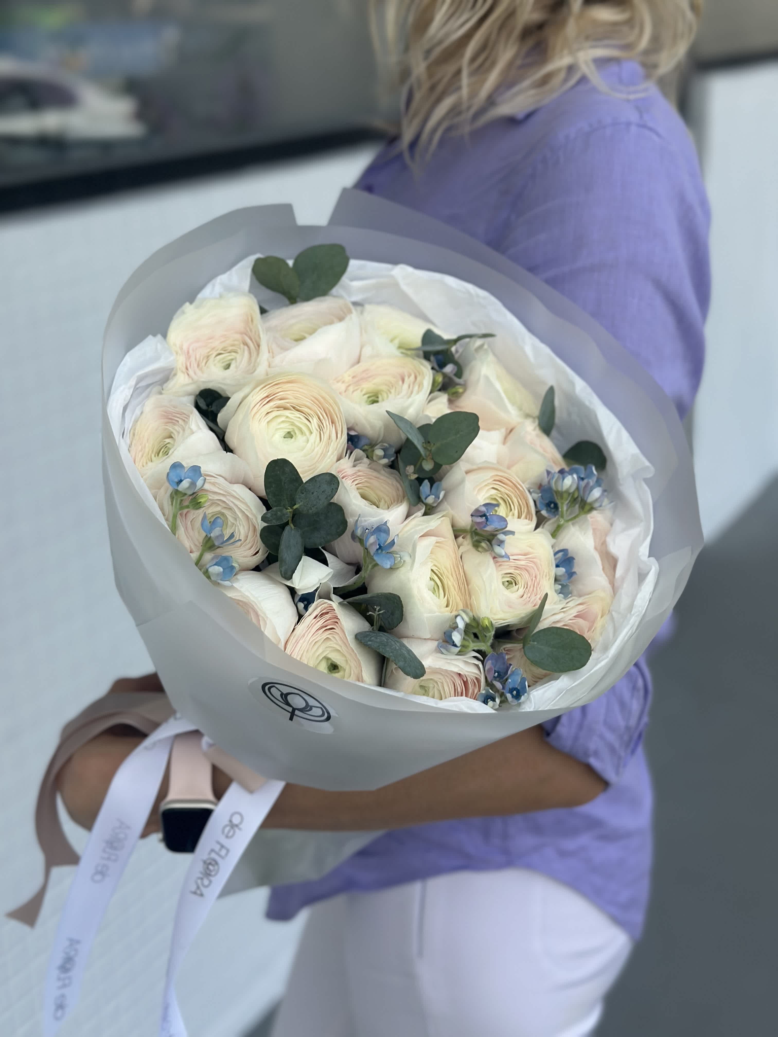 Vanilla Sky - A dreamy arrangement of soft cream ranunculus with the faintest blush at the center, accented by sprigs of delicate blue flowers and fresh eucalyptus. Wrapped in crisp white paper and tied with elegant deFLORA ribbon, this bouquet radiates sophistication and gentle romance — perfect for expressing love, gratitude, or celebrating life’s sweetest moments.