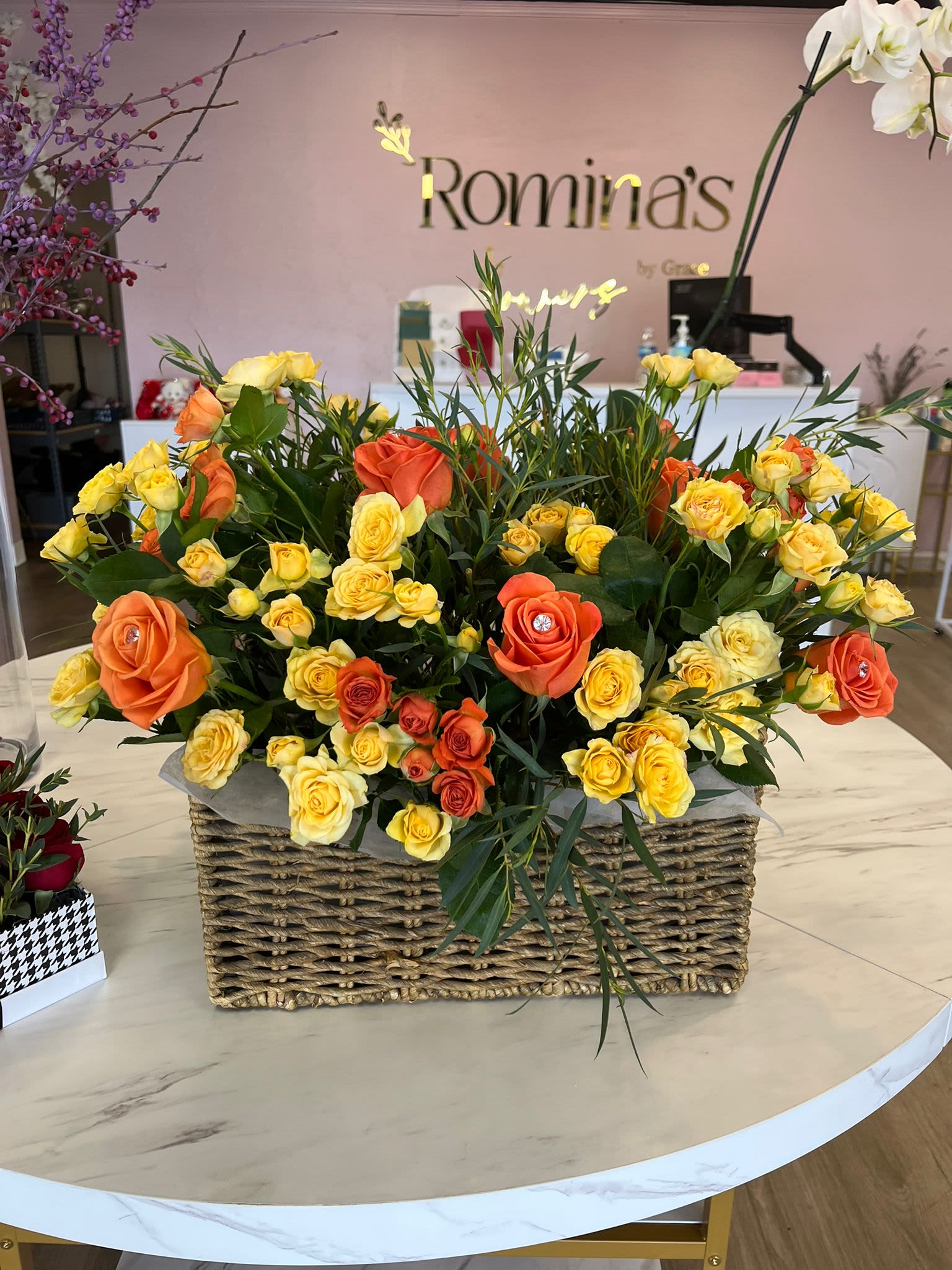 Cecilia - A charming basket arrangement combining mini yellow and orange roses, enhanced with fresh and delicate companion flowers, along with the scent and texture of eucalyptus. This vibrant and cheerful arrangement is perfect for filling any space with color and freshness or for giving as a gift with a warm, natural touch.  Un encantador arreglo en cesta que combina mini rosas amarillas y rosas naranjadas, realzadas con flores de acompañamiento frescas y delicadas, junto con el aroma y textura del eucalipto. Esta composición vibrante y alegre es perfecta para llenar de color y frescura cualquier espacio o para regalar con un toque natural y cálido.  