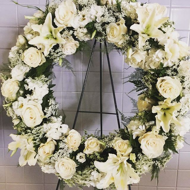 Everlasting - Roses, lilies, and white flowers in a circular wreath, unending and compassionate.   Key notes for this design are a wreath and an easel. If you would like to specify a color scheme, please leave us a note in the Florist Instructions field of your order when you check out.
