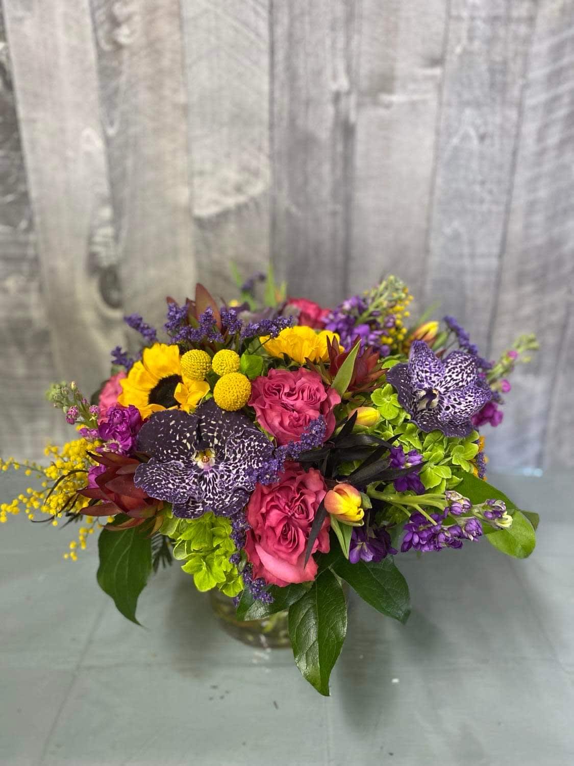 In Vivid Color - An explosion of bright, vibrant colors in our freshest seasonal blooms. Our designers created this with Vanda orchids, garden roses, sunflowers, hydrangea, tulips and more to create a brightly colored harmony of blooms.  Photo is of the standard size.