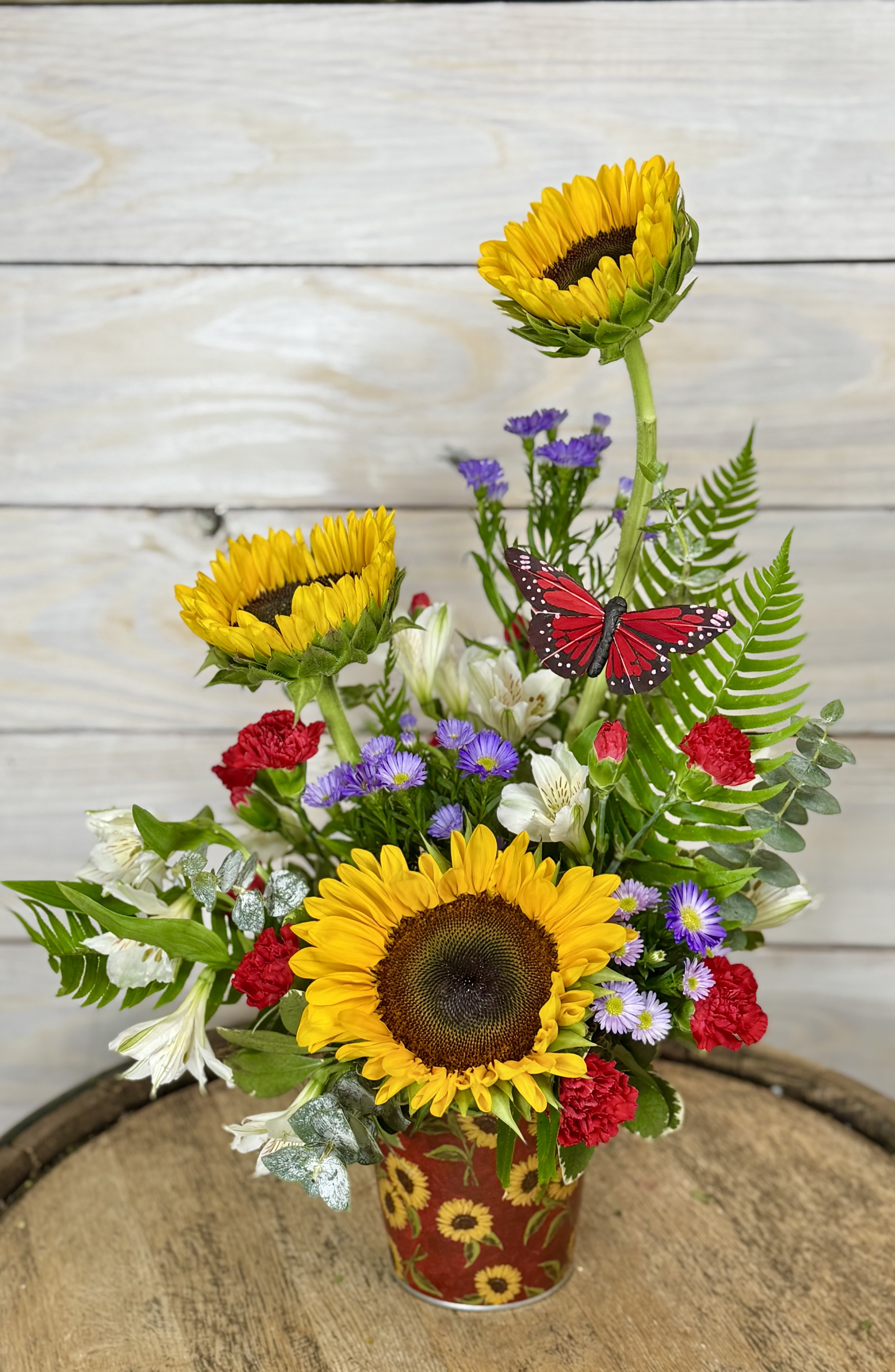 Last Rays of Summer - Bright and sunny sunflowers paired with pops of red, purple and white give this the perfect late summer vibes. These bountiful blooms come in a sunflowers and red themed tin bucket.
