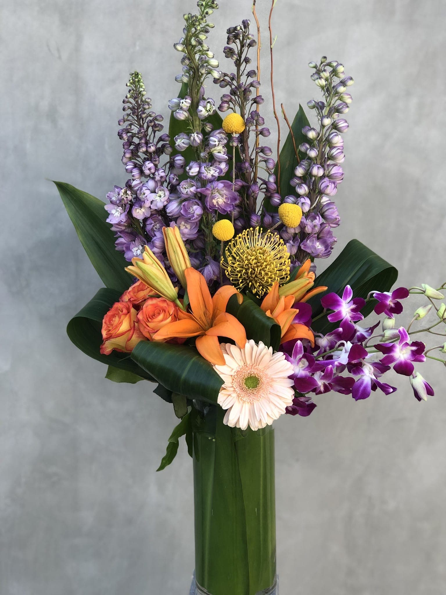 Purple Passion  - Beautiful purple delphiniums, orchids, tiger lilies, proteas. Arranged in a tall glass vase filled with ti leaves. 