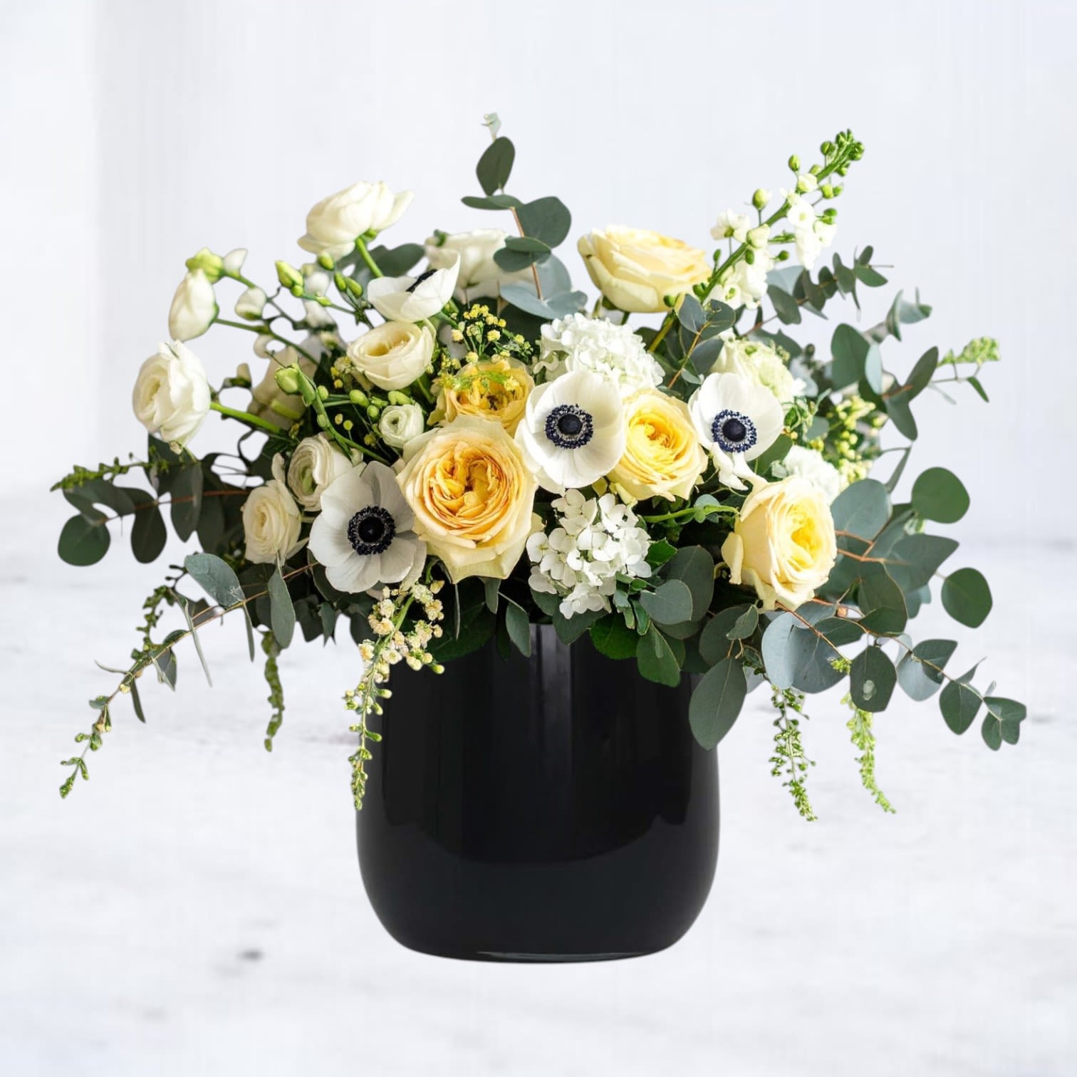 Moonlace - Moonlace is a poetic blend of light and shadow, featuring soft yellow roses, lush ranunculus, and striking white anemones with midnight centers nestled in a black vase, this arrangement evokes elegance with a modern edge. Perfect for sympathy gestures, anniversaries, or to elevate any space with timeless grace. Moonlace delivers a statement of quiet strength and refined beauty.  Available for same-day flower delivery in Houston, Magnolia, Montgomery, and surrounding areas.  