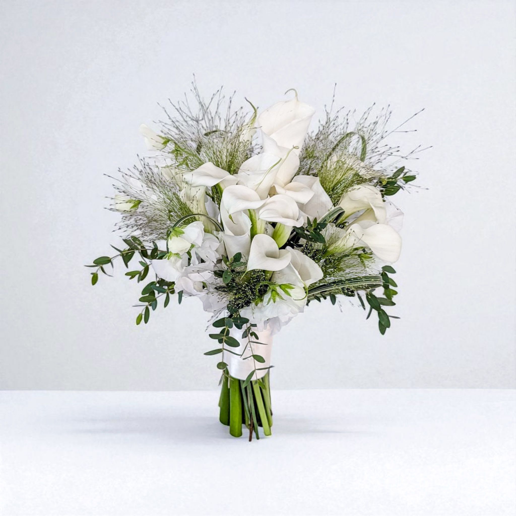 Modern Muse Modern Muse - This is not your typical calla lily bridal bouquet. Designed in a freeform, airy style, it combines pristine white callas with hand-selected textural accents for a modern, one-of-a-kind look. Perfect for the bride who loves timeless flowers but wants a fresh, fashion-forward twist. Includes a matching calla boutonniere for the groom.