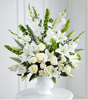 Forever Ours Forever Ours - This Arrangement is a brilliant expression of peace and soft serenity. White roses, carnations, gladiolus, stock and Oriental lilies are accented with the bright green stems of Bells of Ireland and a gorgeous assortment of lush greens, while seated in a designer plastic urn to create a beautiful way to honor the life of the deceased.