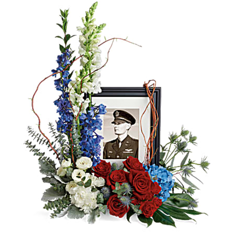 The Always With Us Photo Tribute Bouquet The Always With Us Photo Tribute Bouquet - Surround a beloved picture with patriotic spirit with this gorgeous bouquet of blue hydrangea and red and white roses. This bouquet features blue hydrangea, red roses, red spray roses, white spray roses, white carnations, blue delphinium, white snapdragons, blue eryngium, dusty miller, curly willow, spiral eucalyptus, parvifolia eucalyptus, aralia leaf and lemon leaf. Arrangement does not include picture frame. Orientation: One-Sided