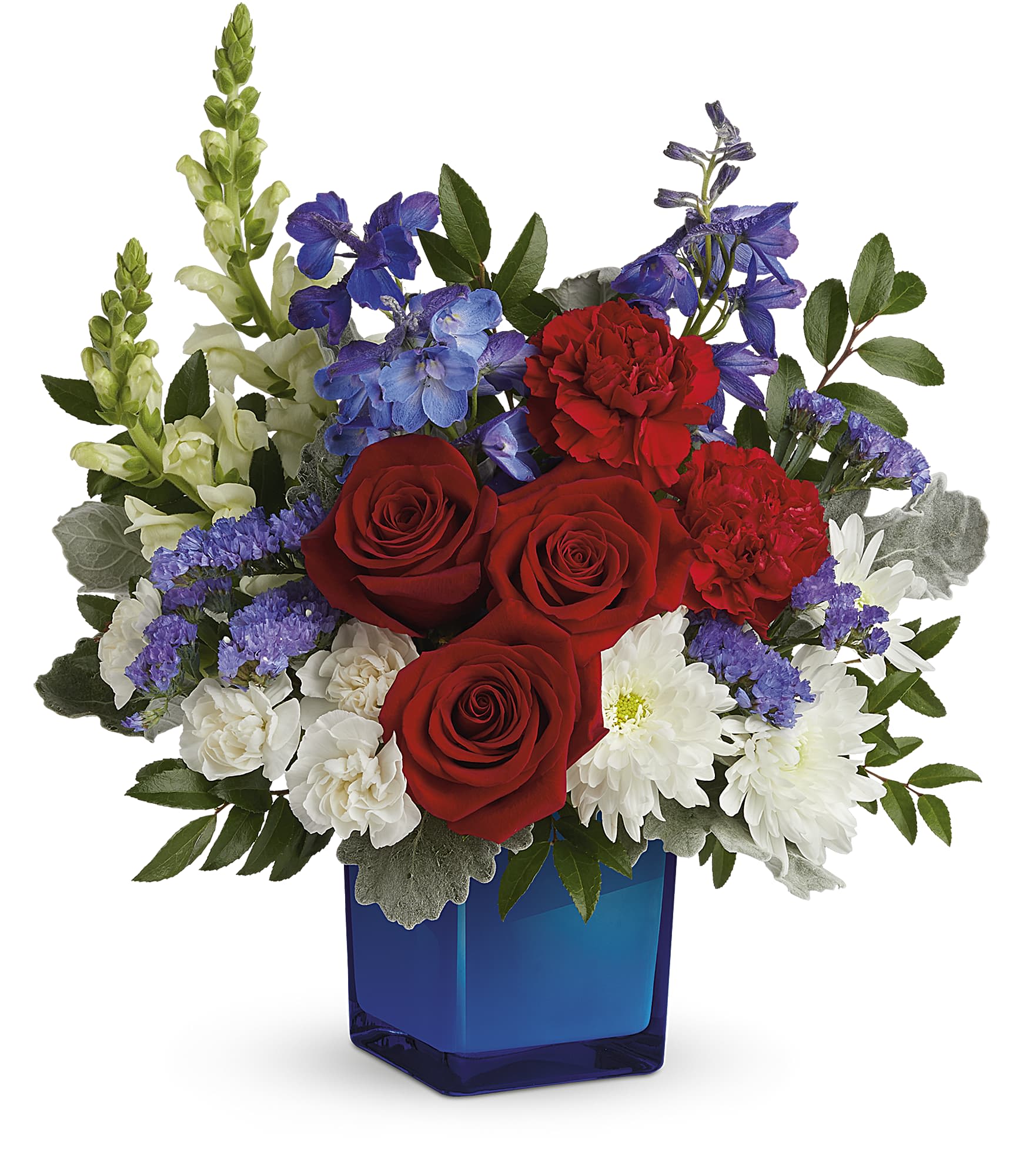 Teleflora's Red, White, &amp; Blooms Bouquet - The classic color trio looks more beautiful than ever in this lush rose bouquet, accented with cool, cobalt glass cube. This red, white, and blue arrangement includes red roses, red carnations, miniature white carnations, blue delphinium, white snapdragons, white cushion spray chrysanthemums, blue sinuata statice, huckleberry and dusty miller. Delivered in Teleflora's Color Splash Cube.