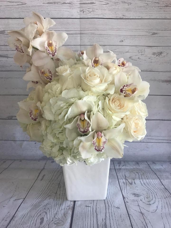 Orchid Cascade - An elegant and modern structural arrangement composed of cymbidium orchids, fresh roses, and hydrangea, in a chic vase. A beautiful choice for anniversaries, romantic surprises, bridal showers, weddings, or any celebration worth remembering!  Container may vary.