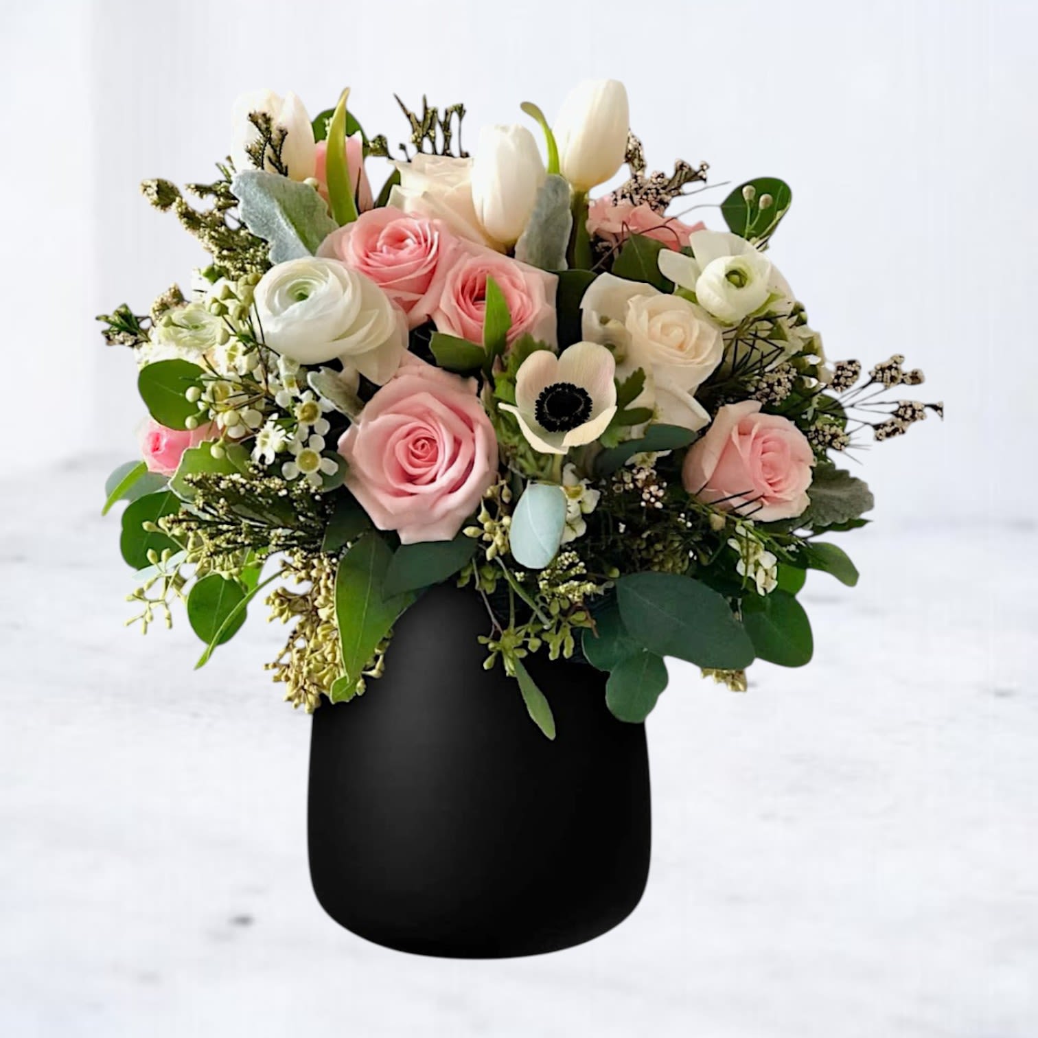 Midnight Bloom Midnight Bloom - Celebrate any special occasion with Midnight Bloom, a stunning floral arrangement that radiates elegance and charm. Featuring delicate blush spray roses, ivory ranunculus, crisp white tulips, and striking anemones, this bouquet is beautifully accented with lush greenery and wax flowers for a soft yet modern aesthetic. Designed in a sleek matte black vase, this arrangement creates a bold contrast that exudes sophistication. Perfect for birthday surprises, milestone celebrations, or sending a chic and timeless floral gift, Midnight Bloom is a breathtaking way to make their day unforgettable. Available for same-day delivery in Houston and surrounding areas, ensuring your thoughtful gesture arrives fresh and full of beauty.