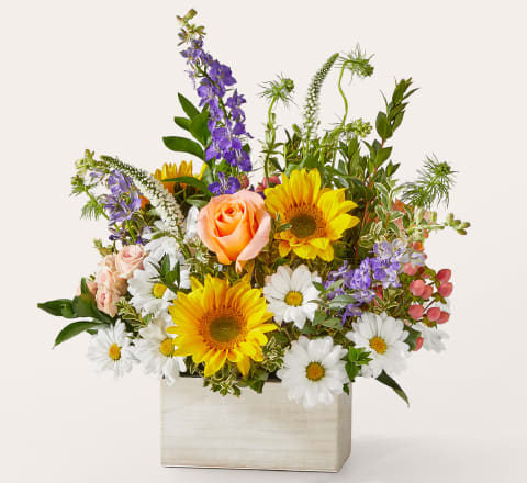 The Good Life Bouquet The Good Life Bouquet - A cheerful mix that feels like sunshine in a vase. The Good Life Bouquet features bright sunflowers, soft pink roses, playful daisies, and lavender larkspur, arranged with fresh greens and seasonal texture in a whitewashed wooden box. It's vibrant, relaxed, and effortlessly charming. Perfect for birthdays, new beginnings, or simply saying “thinking of you.” Approximately 19"H x 16"W.