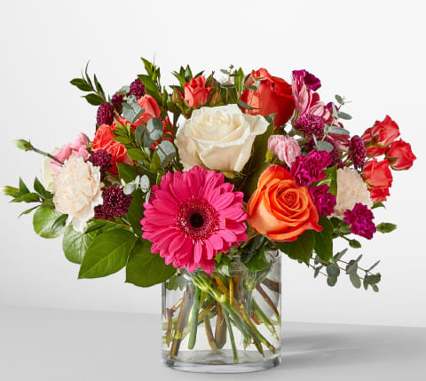 Smell The Roses Bouquet - Smell the Roses Bouquet delights with a rainbow of blooms including Orange Roses, Peach Carnations, and playful Purple Pompons, accented by fragrant Eucalyptus.  Arranged in a classic glass vase, this cheerful mix is perfect for birthdays, thank yous, or bringing a burst of happiness to any day.  Approximate Size: 12&quot;H x 15&quot;W. Order now for fresh flower delivery!