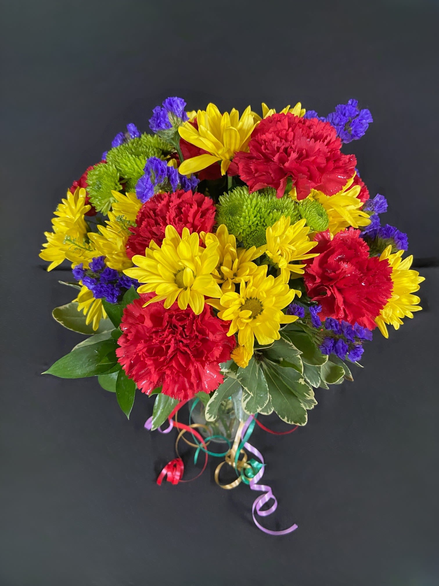 Birthday Bash Bouquet - Celebrate a special birthday in style with this arrangement of yellow daisies, red carnations, green CDN poms, and purple filler.