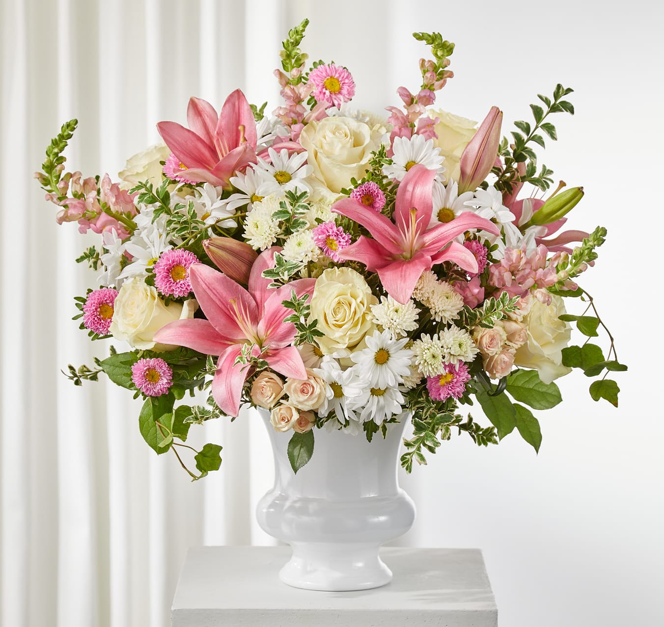 Empathetic Blooms Arrangement - The Empathetic Blooms arrangement is a tender expression of care and compassion. Featuring ivory roses, pink snapdragons, matsumoto asters, lilies, spray roses, and white button pompons with daisies, this bouquet combines soft textures and soothing colors to bring comfort and peace.  A thoughtful choice for offering condolences, celebrating life, or simply sharing heartfelt support.  Approximately 22&quot;h x 23&quot;w