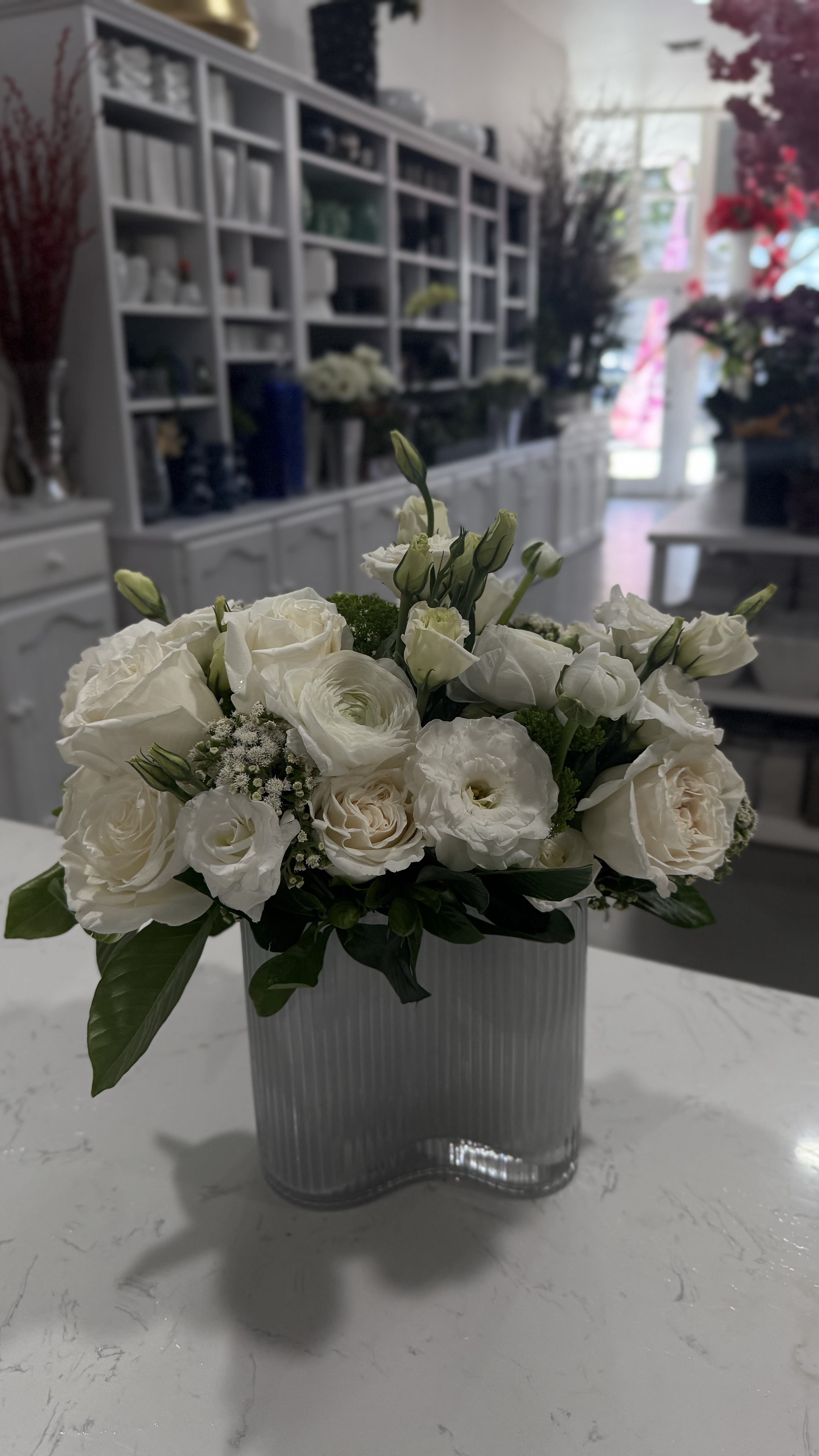 Moonmilk - A dreamy mix of ivory roses, lisianthus, ranunculus, and delicate fillers arranged in a sculptural wave vase. Moonmilk offers a clean, modern aesthetic with a soft romantic edge—perfect for minimalist spaces, serene gifting, or luxe celebrations.