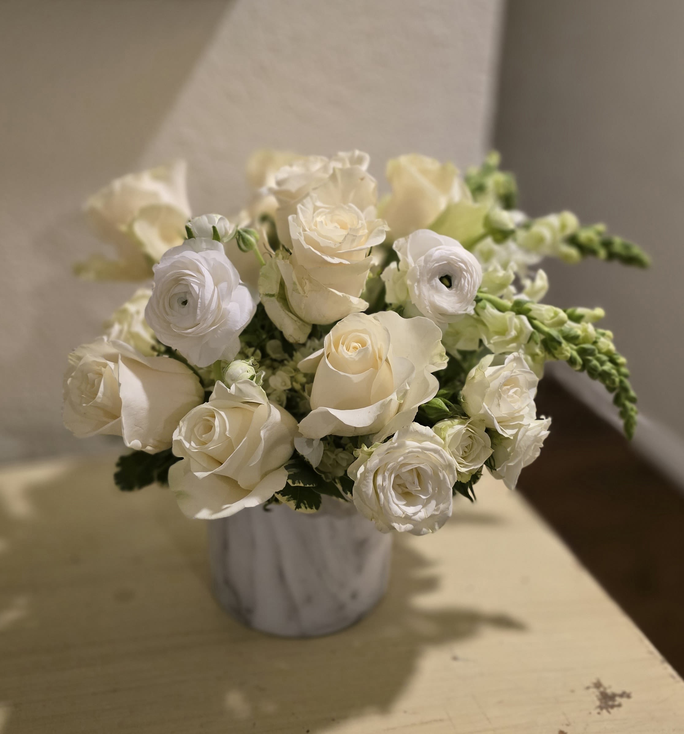 Remember Me - Remember Me is an all-white arrangement of seasonal blooms. Typically includes roses, snap dragons, ranunculus and hydrangeas, but there could be others depending on what is in bloom. This is the perfect gift for sympathy or celebrating a new year, a new baby, or a newly married couple. This arrangement also serves as an excellent centerpiece for corporate events. 