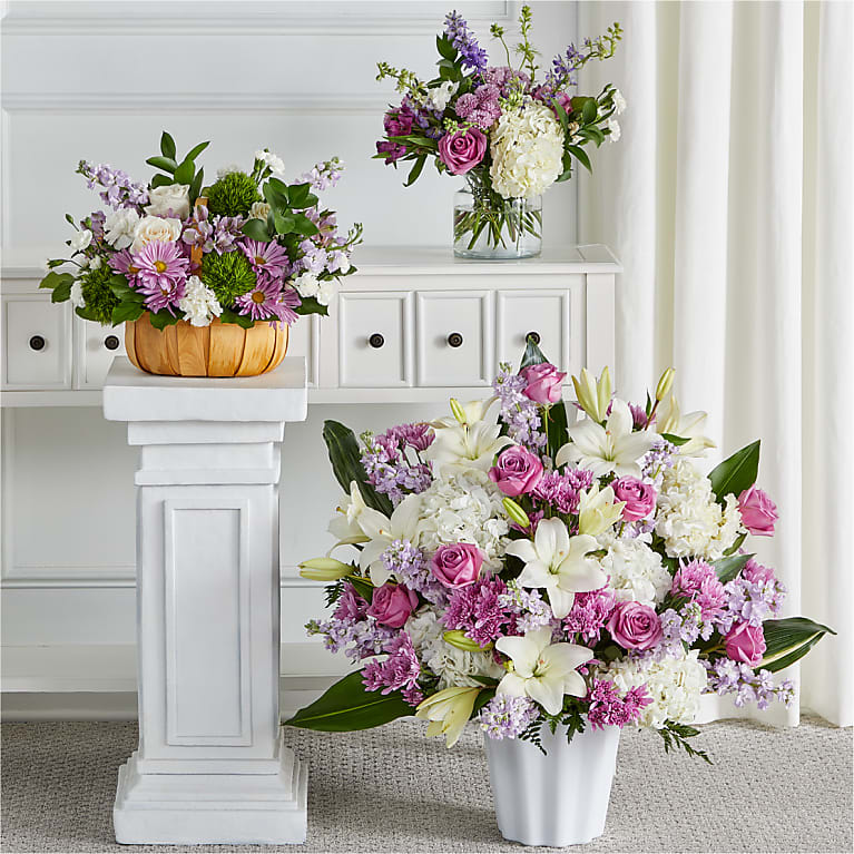 Tender Embrace Bundles - Featuring heartwarming lavenders and whites, the traditional arrangements of this sympathy set are meant for celebrating the life of a loved one at a visitation, funeral, church service, cremation, or cemetery service – or as a delivery to the family's home.  Please Note: The bouquet pictured reflects our original design for this product. While we always try to follow the color palette, we may replace stems to deliver the freshest bouquet possible, and we may sometimes need to use a different vase or basket.