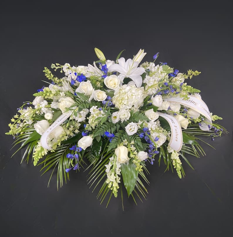 Dark Blue & White Casket Spray Dark Blue & White Casket Spray - A lovely mixture of white flowers such as roses, lilies, hydrangeas, lisianthus, snapdragons, and veronica broken up with stocks of dark blue delphinium. Price includes up to 4 custom printed ribbons.
