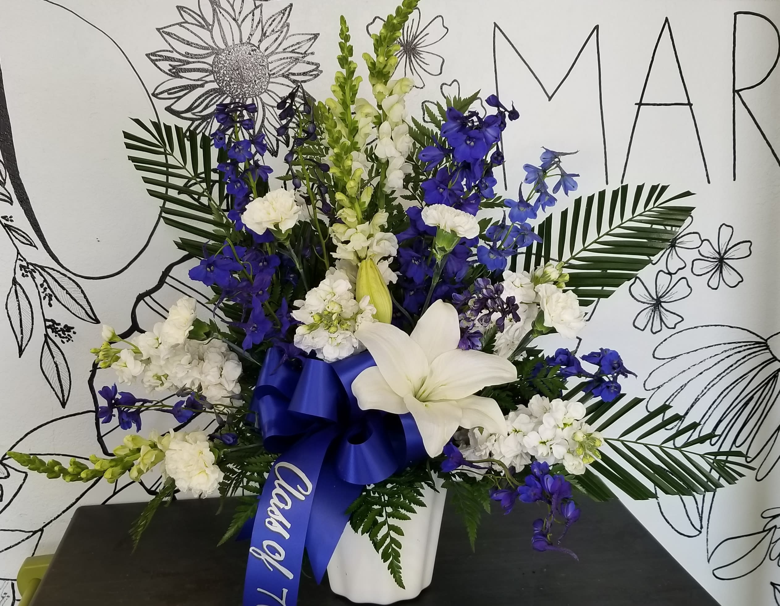 Blue And White Memories - This arrangement brings the memories forward of that special loved one.White flowers mixed with blue delphinium designed with the freshest blooms available. The writing on the ribbon is optional, please leave desired message  in the special instructions section, other wise the ribbon will be blank. Flowers maybe substituted due to availability.