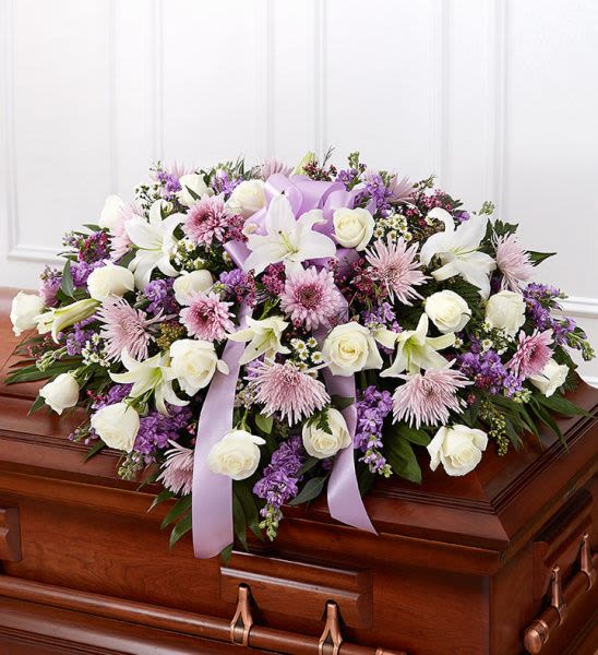 Rose Half Casket In Lavender  - Half casket cover arrangement of white roses, hybrid lilies and monte casino, lavender cremones, spider mums and stock, purple waxflower and fresh greenery; accented with a lavender satin ribbon