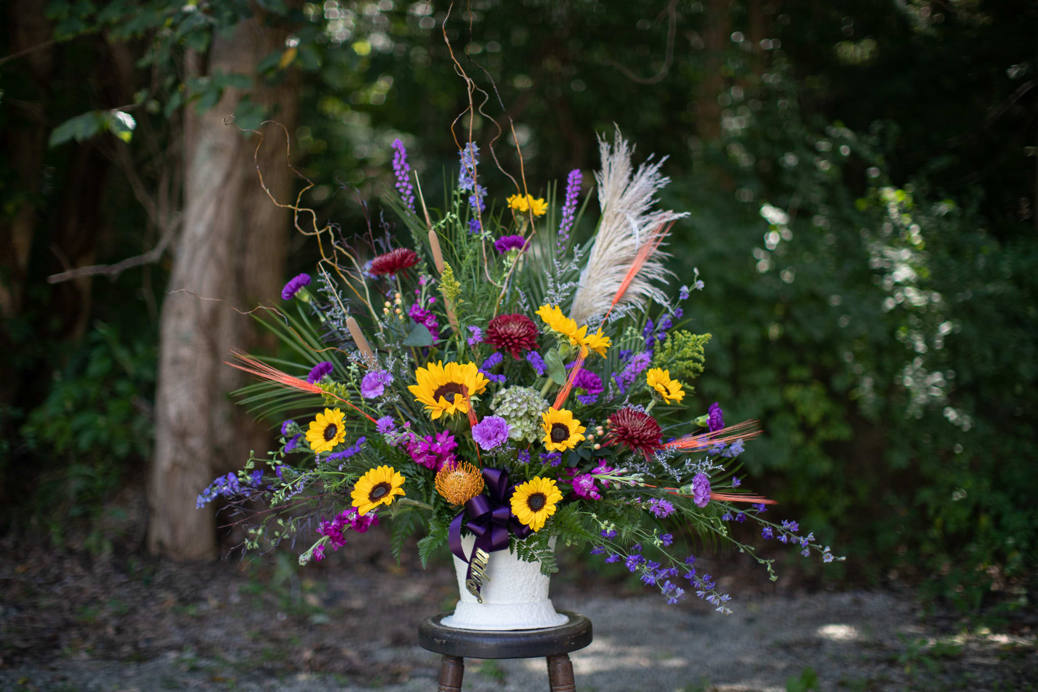 Autumnal Memorial Basket - A one sided large scale basket of seasonal flowers to coordinate the Autumnal Urn Wreath. Blooms may vary in color shades and will be inspired by fall. Photographed at premium price point. Premium size is approximately 3.5 feet in height and 3.5-4 feet at its widest point. Orientation is one sided.   