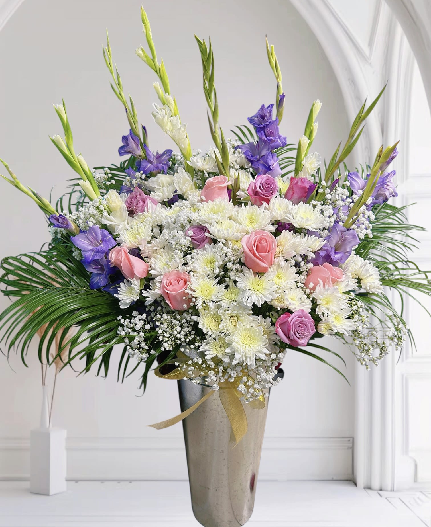Eternal Grace Eternal Grace - A graceful arrangement featuring soft pink roses, lavender roses, and purple gladiolus, accented with delicate baby’s breath and lush greenery. White chrysanthemums add brightness and texture, creating a harmonious blend of romance and elegance. Perfect for expressing love, sympathy, or simply bringing beauty and serenity to any space. Occasions: Ideal for birthdays, anniversaries, sympathy gestures, or as a refined centerpiece for special events.
