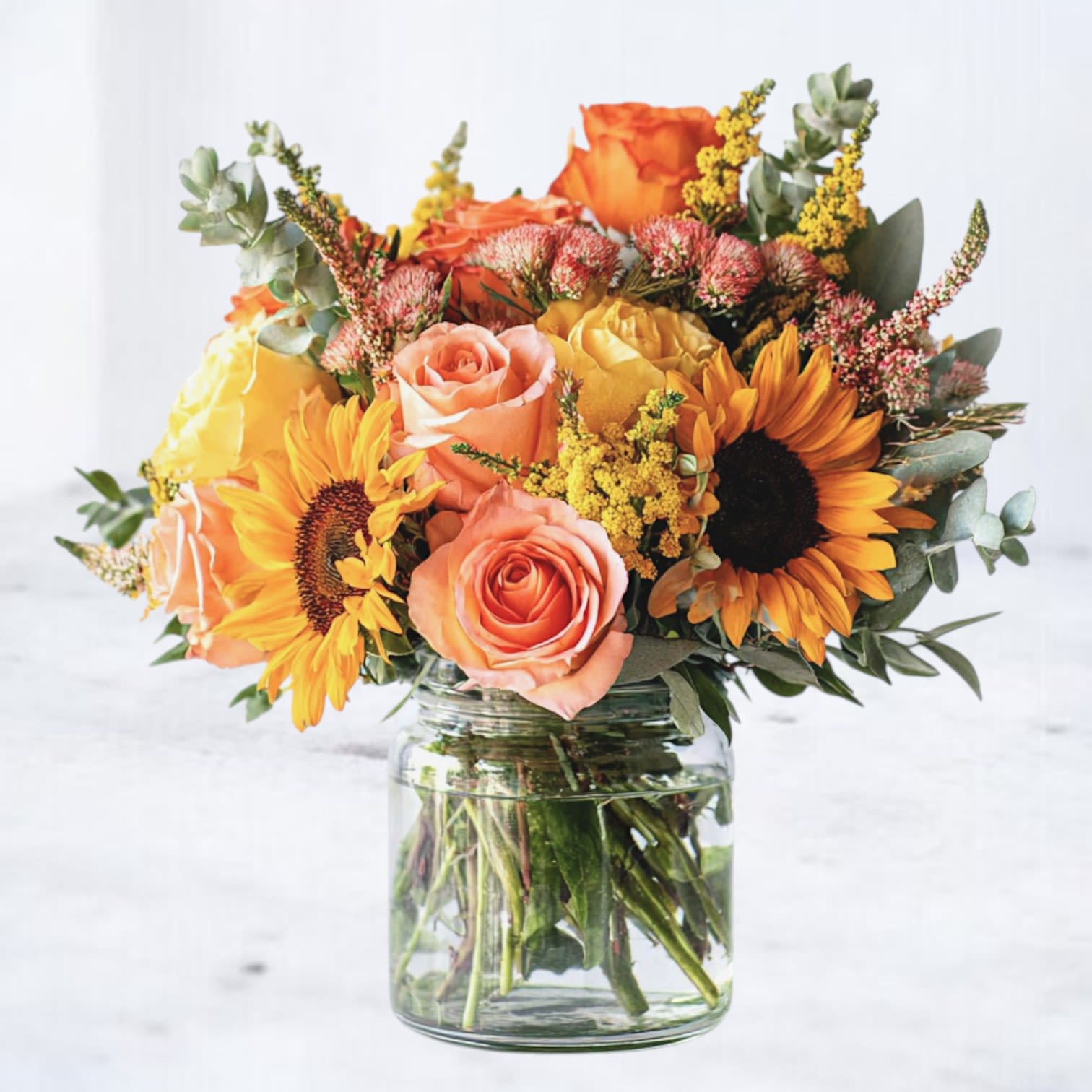 Golden Petal Symphony - Brighten any space with the Golden Petal Symphony, a radiant mix of sunflowers, peachy roses, vibrant ranunculus, and cheerful yellow alstroemeria. Accented with fresh greenery and seasonal blooms, this lush arrangement brings warmth and joy to any occasion. Available for same-day delivery in Houston and surrounding areas, this bouquet is a testament to nature's vibrant palette. 