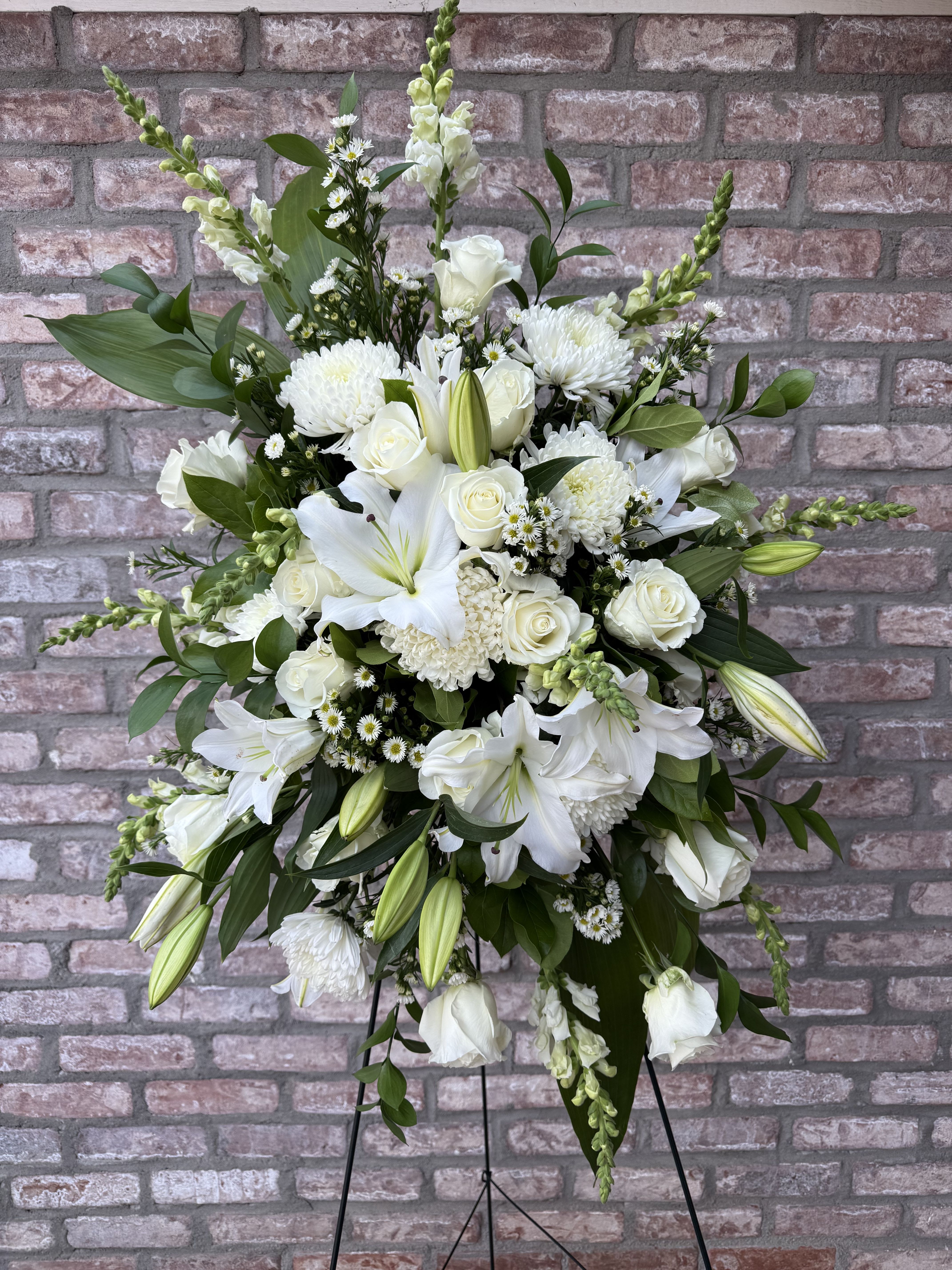 Eternal Grace Easel Tribute Eternal Grace Easel Tribute - Eternal Grace – A radiant all-white standing spray featuring lilies, roses, and snapdragons, symbolizing purity, peace, and everlasting love. Thoughtfully designed to honor a life well-lived and reflect the comforting promise of eternal families and heavenly reunion. Stands approximately 36” tall, 30” wide. Comes with a 60” easel.