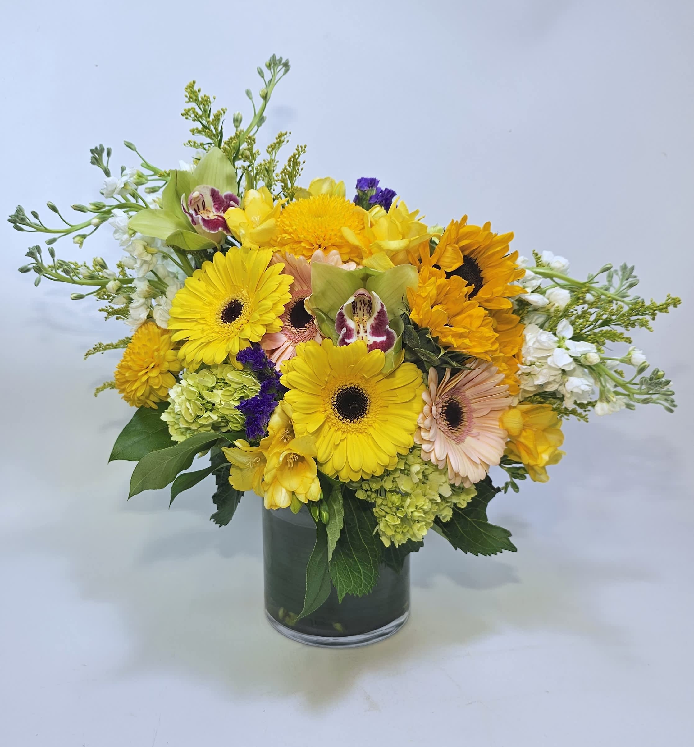 Flutter By - Keep your days sunny and bright with our Flutter By bouquet! This bouquet is packed with bright and vibrant colors to bring cheer and sunshine into anyone's day. Filled with gerbera daisies, hydrangea, statice, and fillers. Perfect for a gift, home centerpiece, or any occasion!