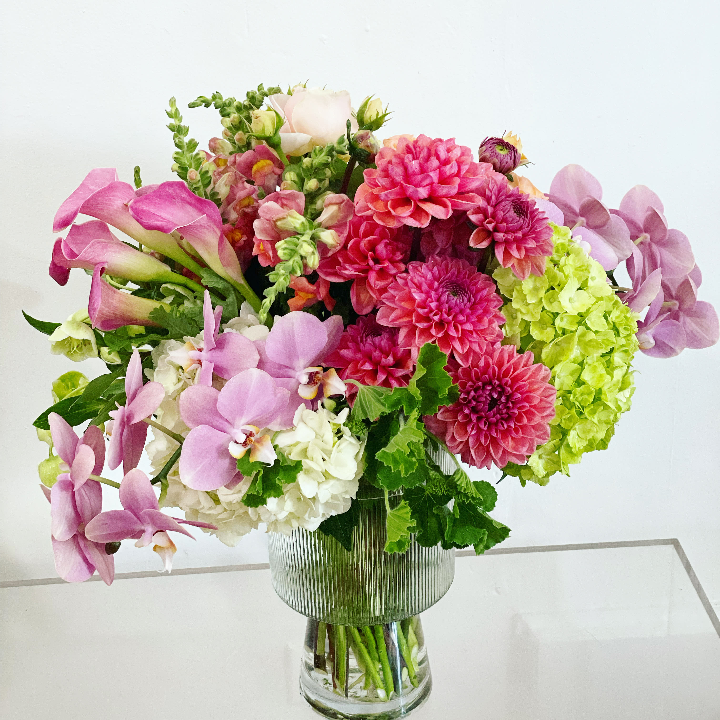 Lovely Day  - 415 751 2747  Watermelon pinks, white, and green florals in a chalice vase. Elegant and impactful, this is a premium bloom bouquet that will delight the recipient. It is happy and people LOVE receiving this design.   The picture is meant to represent they style and color palette of what we will send out on your behalf.  NOTES: We will choose the freshest and most interesting ingredients at the market to make this arrangement shine. Vessel may be substituted depending on availability.    If any design element such as color or flower/foliage are very important to your order please contact us to ensure availability first by calling the shop at  415 751 2747   