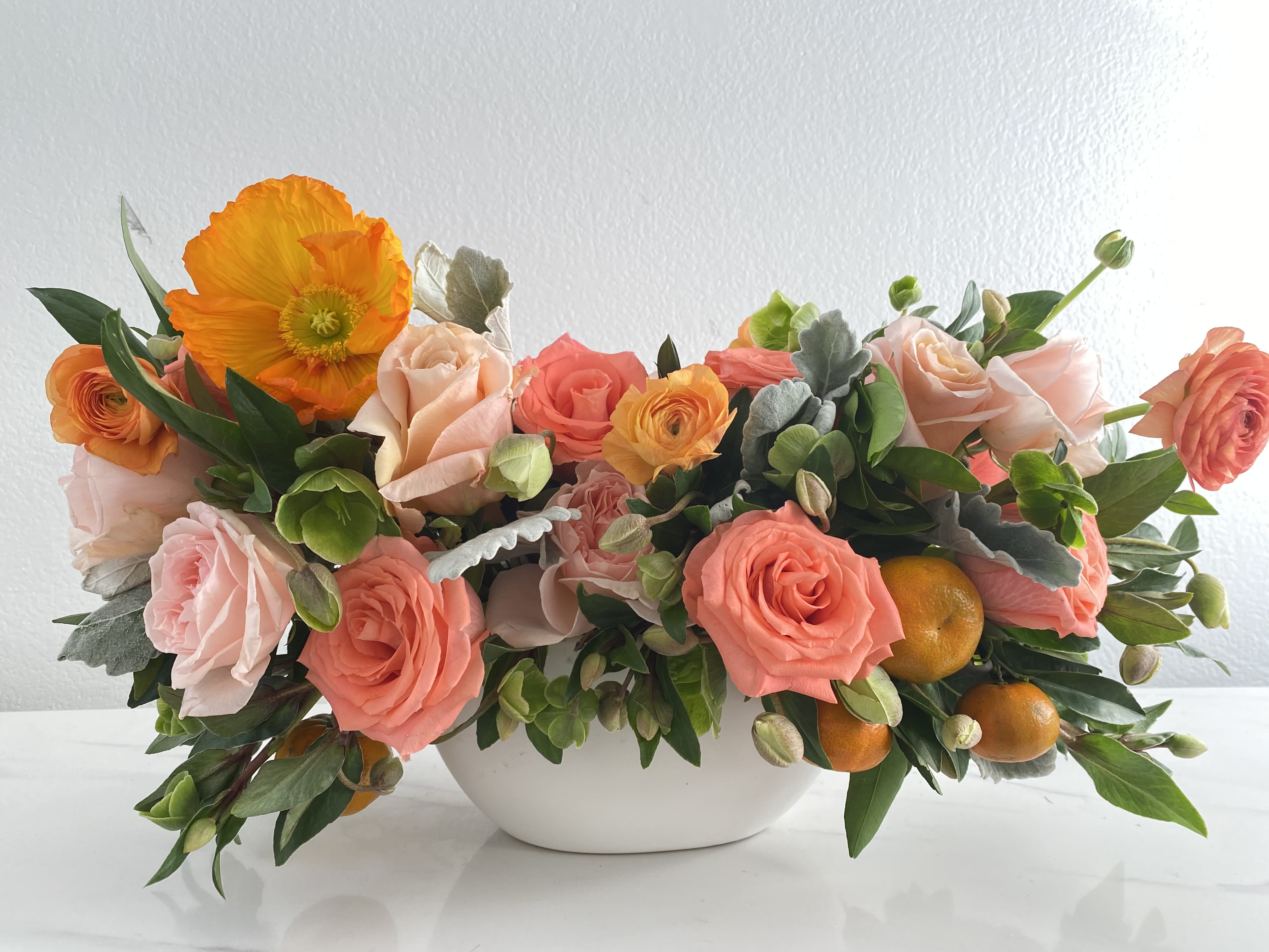 Tangerine Fiore - Lush arrangement in 10&quot; wide boat vase filled with salmon and peach roses, peach ranunculus, orange poppies, hellebores, and kumquats.
