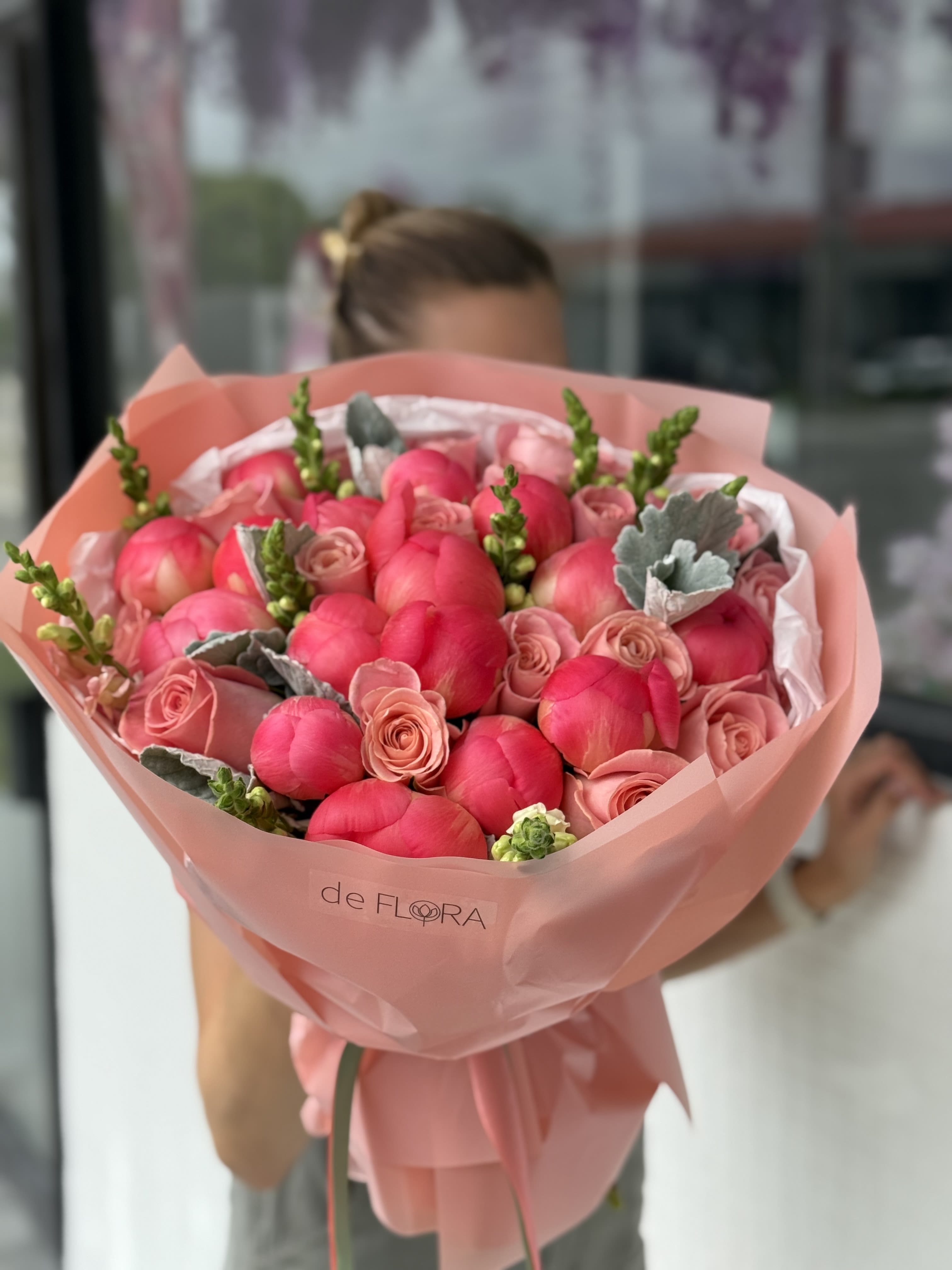 Coral Embrace - Wrap your emotions in elegance with our Coral Embrace bouquet — a stunning fusion of deep coral peonies and blush garden roses, kissed with velvet-silver dusty miller and playful green snapdragons. Each bloom is hand-selected and artfully arranged in our signature soft pink wrap to create a lush, romantic statement.  Perfect for anniversaries, grand gestures, or simply saying “You’re unforgettable.” Includes a greeting card, flower food, and free delivery in our elegant gift box.