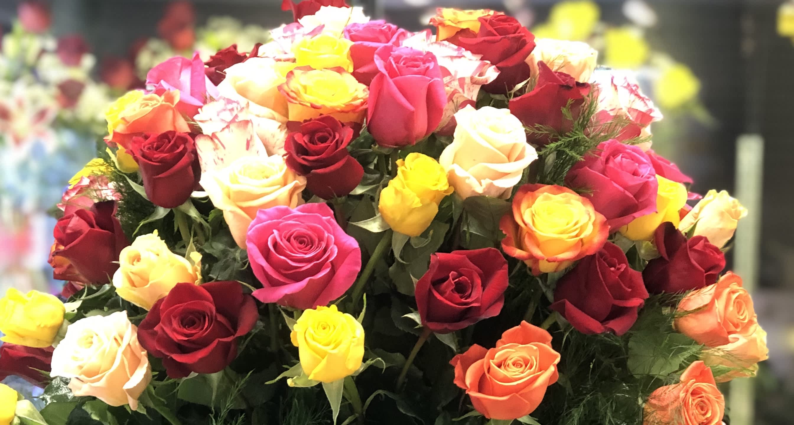 Love's Truest Language Love's Truest Language - This vibrant arrangement features 50 multi-colored roses, accented with fresh greenery, creating a joyful and colorful display.