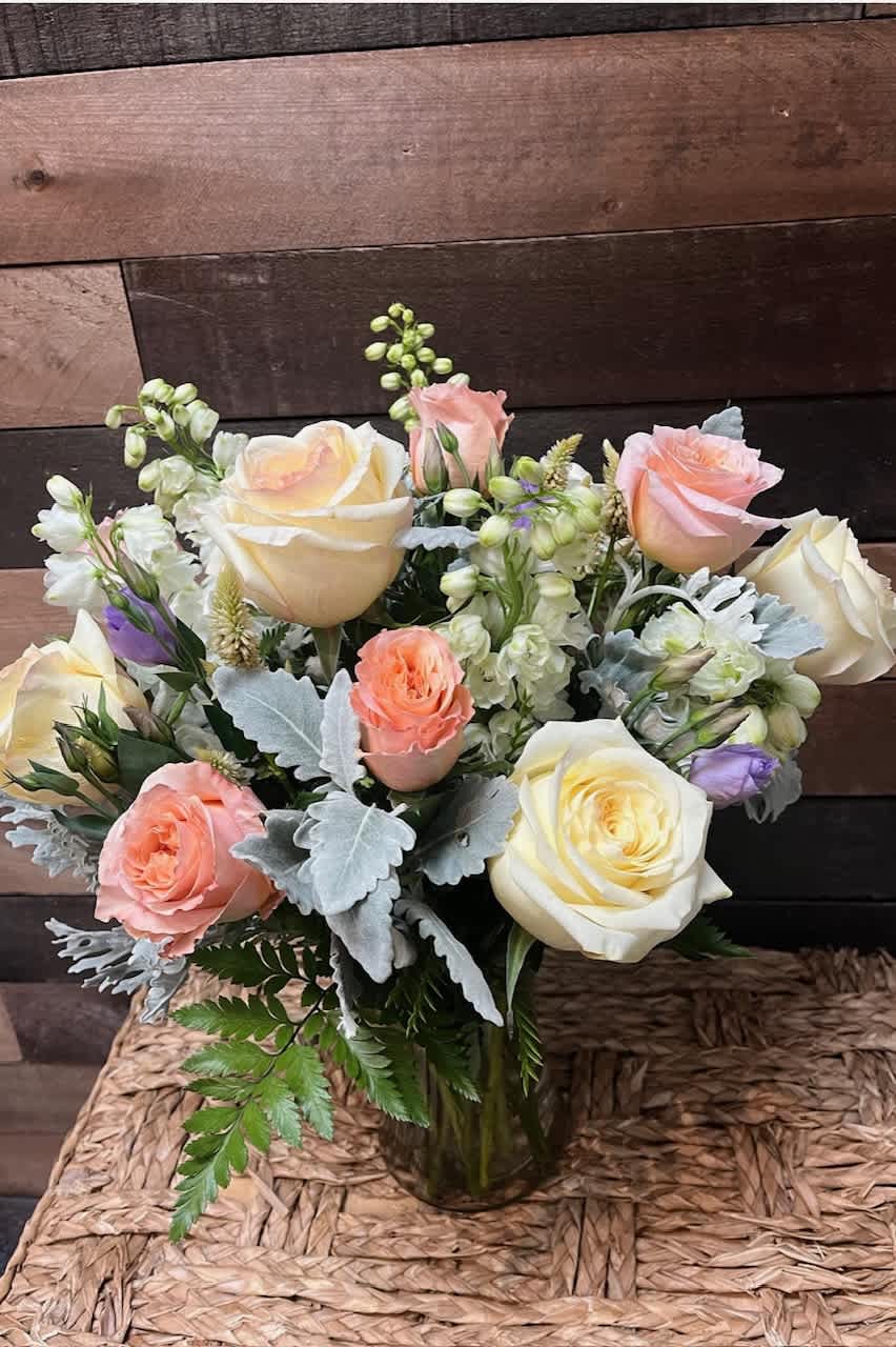 Enchanted Garden Enchanted Garden - The "Enchanted Garden" arrangement features peach and white roses, complemented by delphiniums and stock, set against a backdrop of lush greenery for a whimsically elegant display.