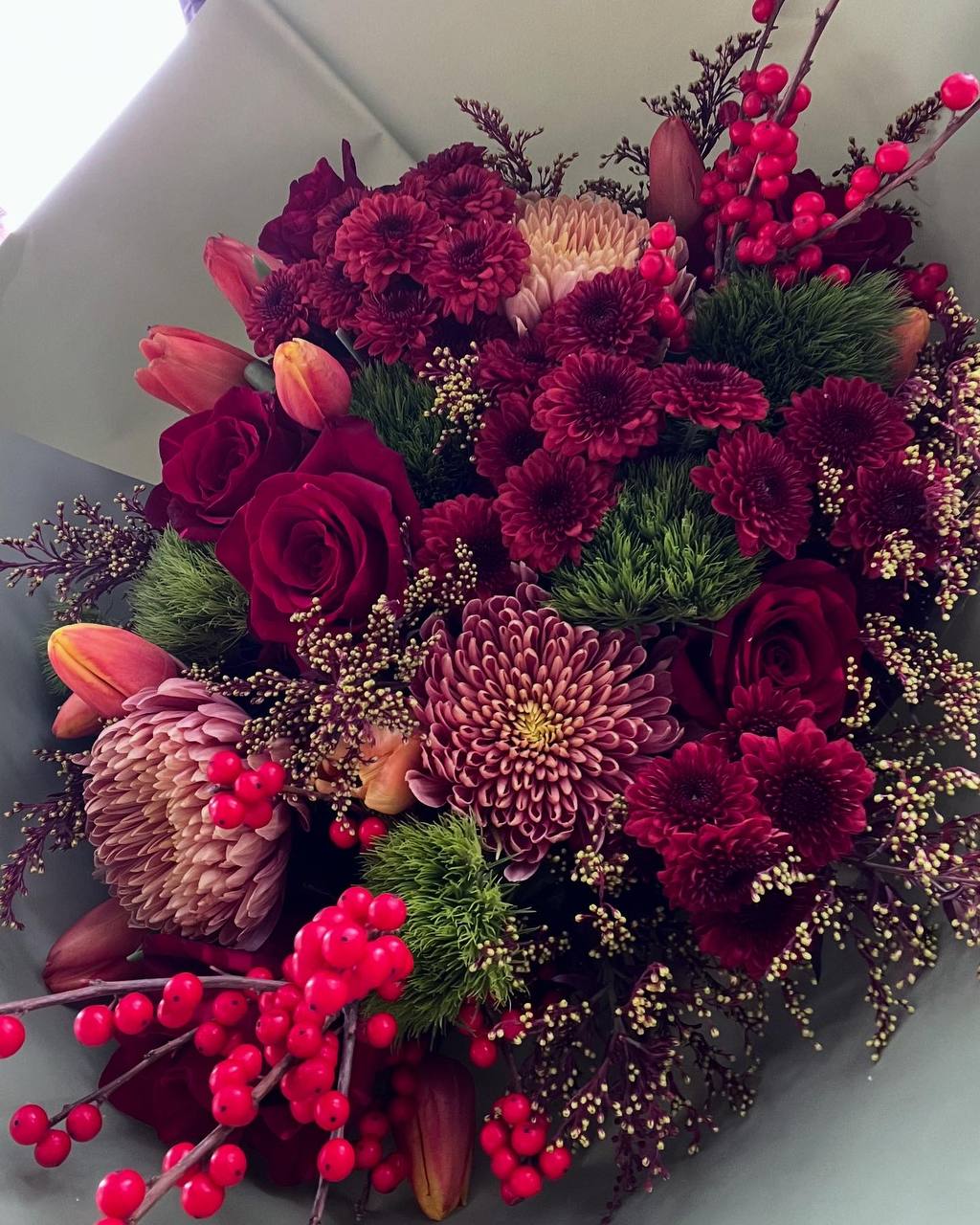 Scarlet Symphony  - Scarlet Symphony – A Melody of Passion and Elegance  A breathtaking arrangement where deep crimson hues harmonize with rich textures, creating a luxurious and dramatic composition. The lush red roses, vibrant chrysanthemums, and delicate tulips blend seamlessly with festive berries and fresh greenery, evoking warmth, passion, and sophistication. This bouquet is a true statement of love, celebration, and timeless beauty.