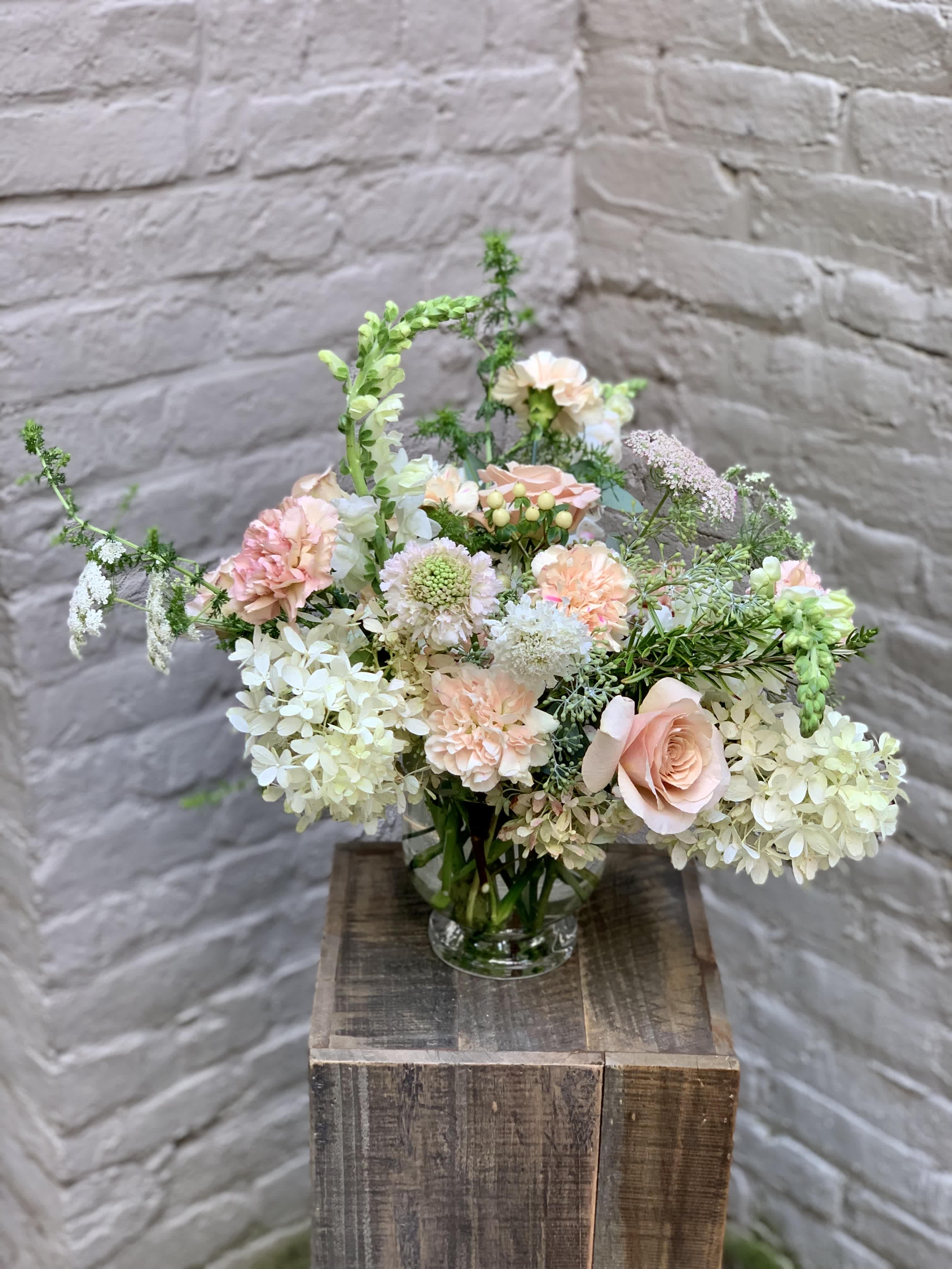 Roussanne - The intriguing and elegant Roussanne. With its monochromatic beauty and complex textures, this arrangement features powdery beige roses, ruffled antique mauve carnations, and creamy white hydrangeas in a modern clear glass vase.  Subtle aromas of sugar and clove; delightful as a sweet summer day. 