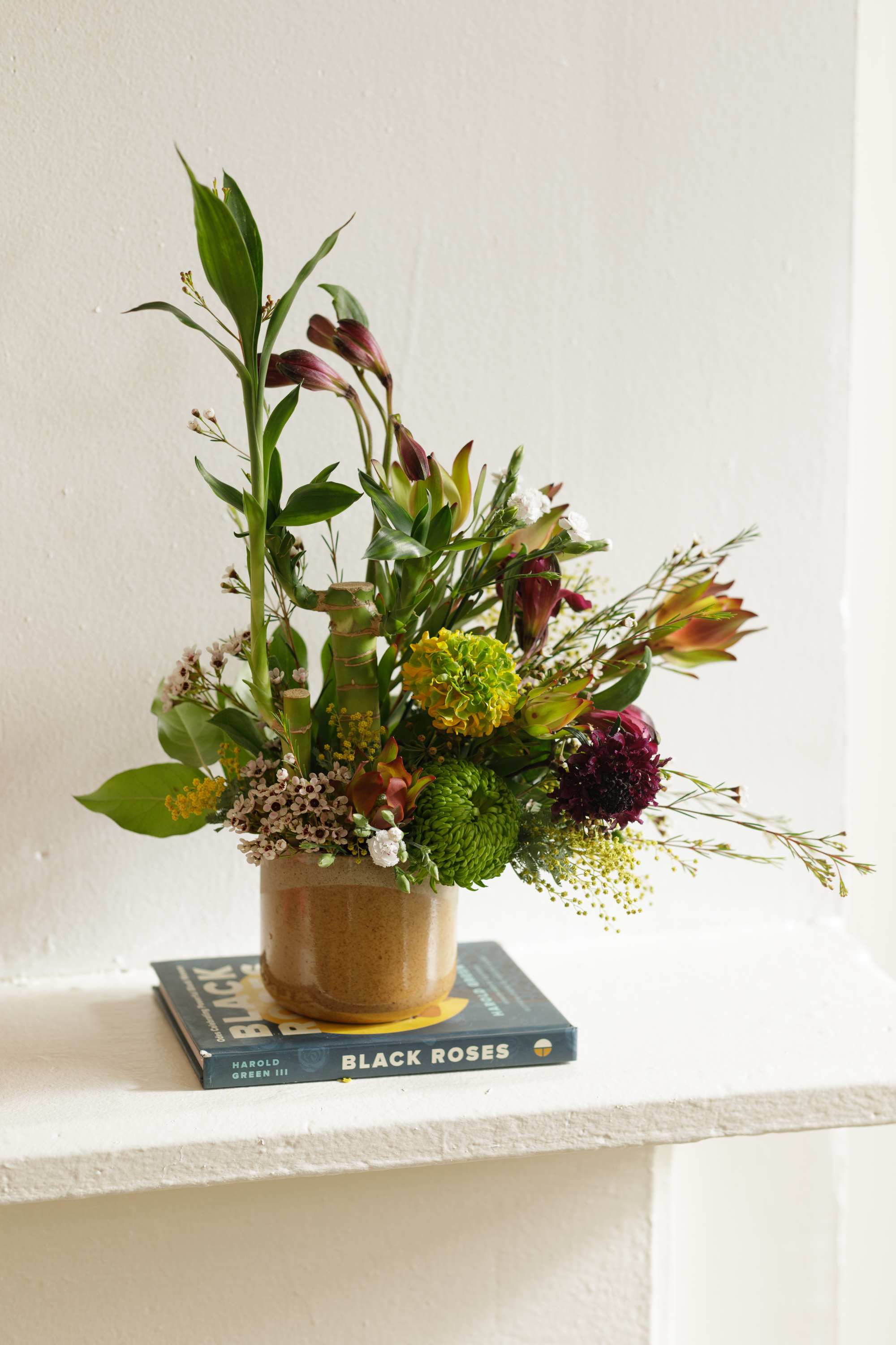 Bamboo &amp; Blooms Collection: The Sutter  - The Sutter is our petite-sized modern arrangement created in a ceramic vase. By using Lucky Bamboo and pairing with complimenting blooms this design is sure to be a sculpturally engaging arrangement for any space. Once the flowers have gone through it's life cycle enjoy the Lucky Bamboo in a beautiful vessel.   Each of our custom designs is created using fresh curated seasonal blooms. Designers will choose from a unique array of flowers and Lucky Bamboo to create an arrangement tailored for you. Just as no two people are alike so are our arrangments. For special floral requests please place order 4 days prior to the desired delivery date.    **Please note that Brooklyn Blooms move with the seasons, vessels, blooms, and foliage will vary from what you see in the photo. However, it will have the same beauty, uniqueness, and funky style. Please let us know in the florist notes if you have any color preferences, special requests, or love what's in the photo, otherwise, the Bloomies will make a tasteful decision for you! **  ***ALL SPECIAL REQUESTS MUST BE SPECIFIED IN THE FLORIST NOTES SO THAT OUR BLOOMIES ARE AWARE AND CAN DELIVER THE BEST SERVICE. COMMUNICATION IS KEY!!****  Upgrade Notes: Please note that with each upgrade the Bloomies will choose a mix of blooms, premium foliages, and filler to enhance your arrangement for the best presentation!  