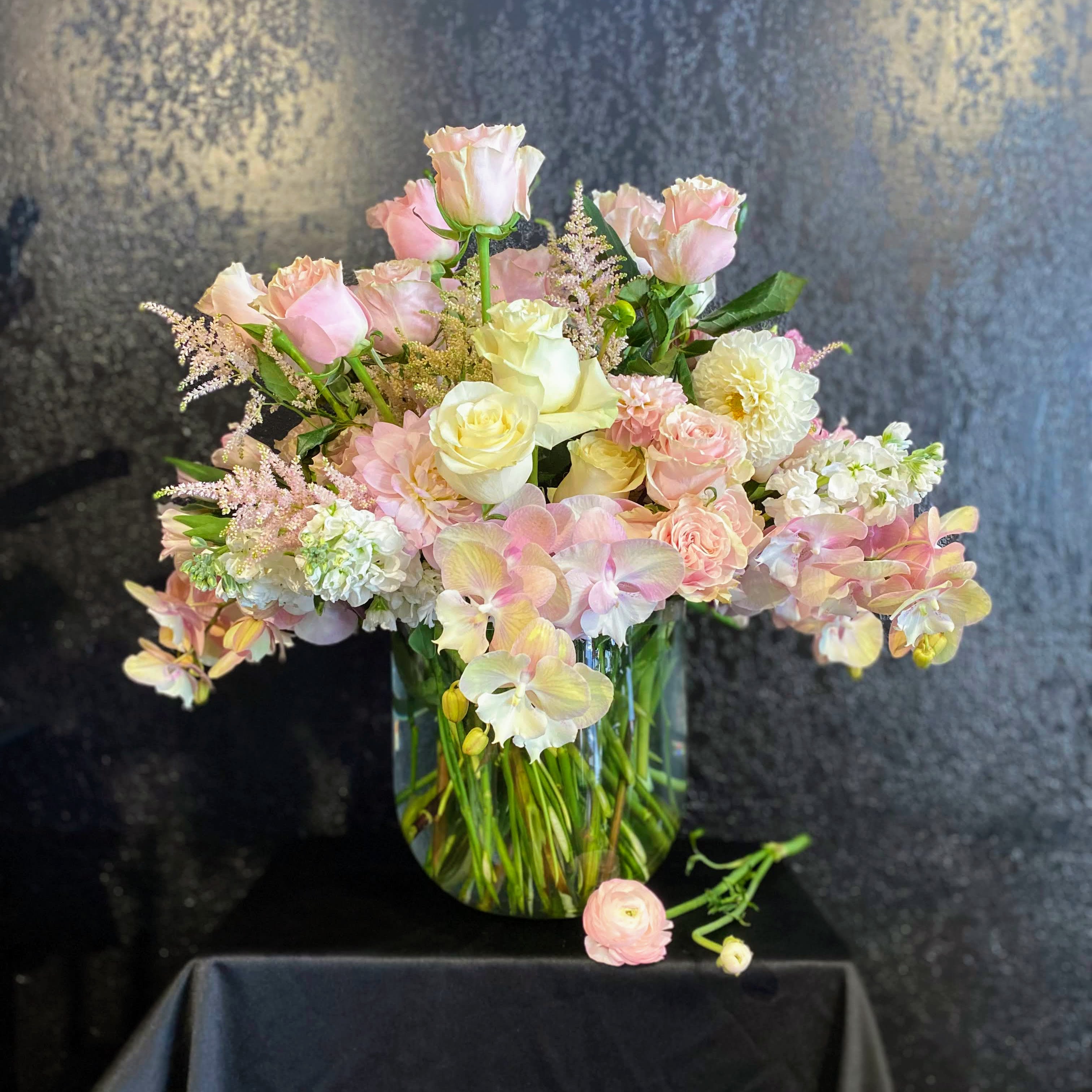 Demure - The only thing Demure about this baby is the color palette!  A most luxurious design of gorgeous seasonal flowers in soft pinks and whites mounded over our favorite curved-bottom cylinder measuringly roughly 9x9&quot;