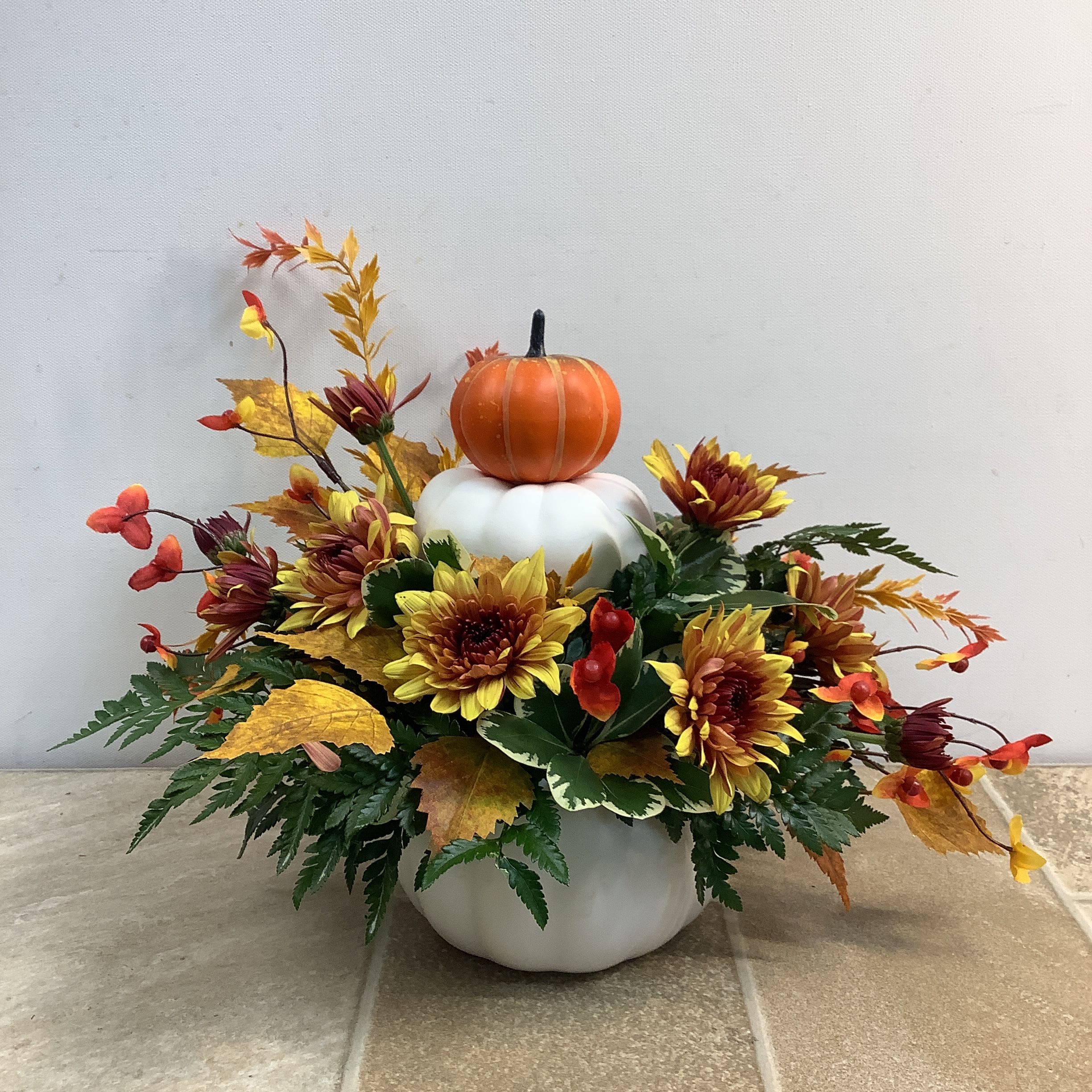 Pumpkin Pile Up Pumpkin Pile Up - Our Pumpkin Pile Up bouquet is a fun and festive autumnal mix of fresh chrysanthemums, silk birch leaves and bittersweet. A white ceramic pumpkin pot is the foundation for this charming arrangement. It’s pretty all around and measures 15” wide x 12” high.
