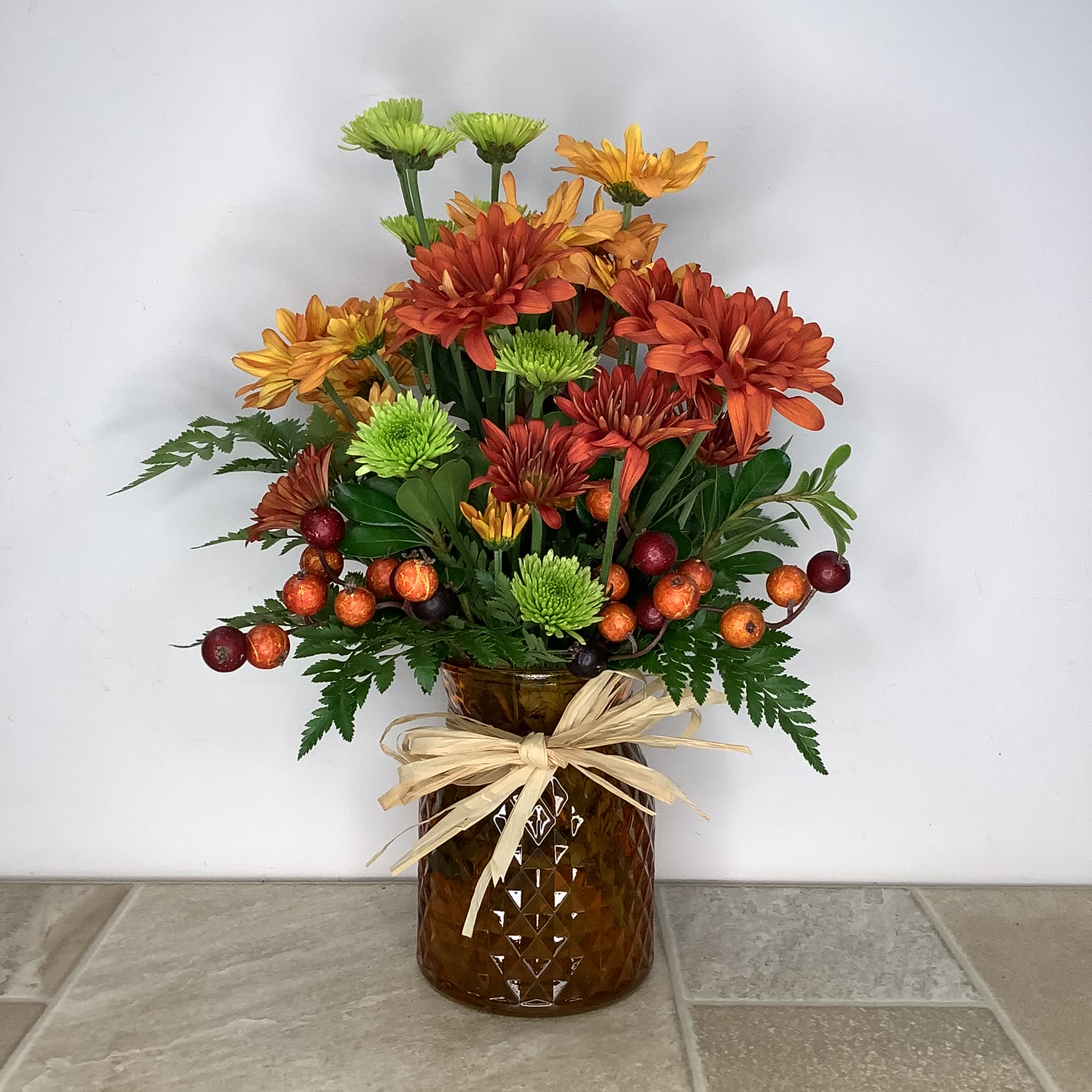 Talia - Chrysanthemums are always a long lasting fall favorite. This pretty bouquet features fresh bronze, gold and green mums decorated with silk berries in an attractive faceted glass vase. It’s 12” wide x 16” tall. 