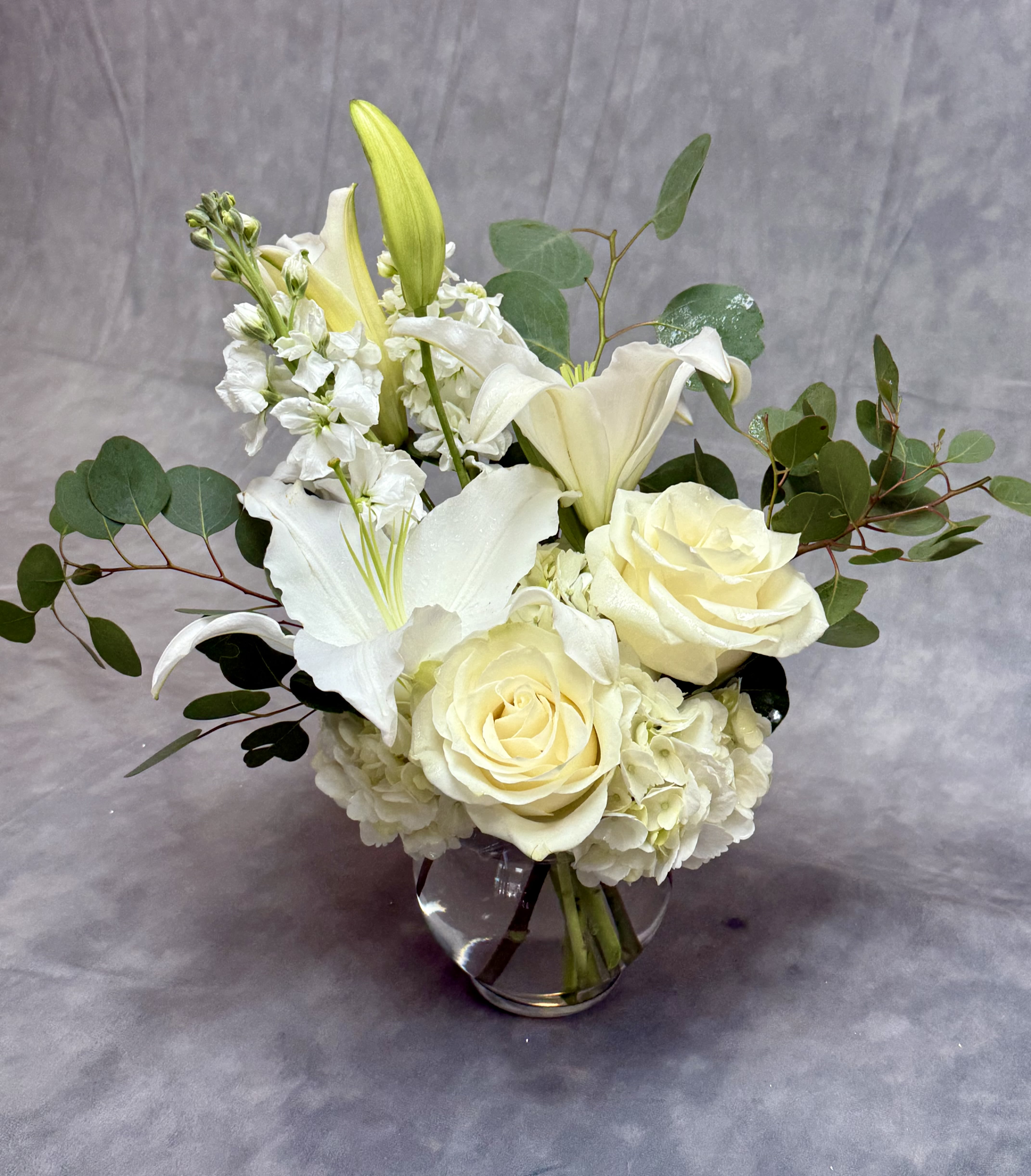 Sweet Thoughts White Vase - This arrangement includes white roses, white asiatic lilies, white stock, and dusty miller. Send your condolences with Sweet Thoughts.   APPROXIMATE DIMENSIONS:10&quot; H X 11&quot; W X 11&quot;L