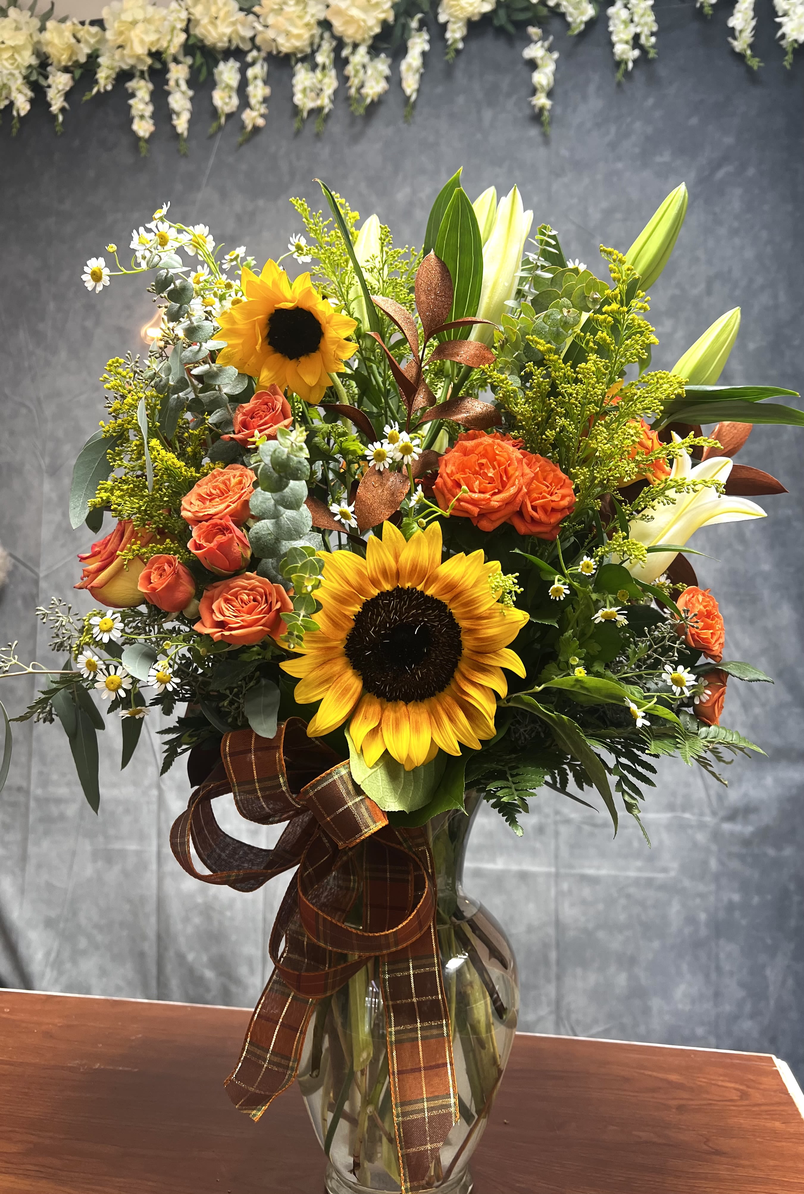 Fall Elegance  -  Celebrate a special birthday with our premium fall vase! This gorgeous arrangement features sunflowers, roses, spray roses, lilies, and more, all beautifully tied together with a festive fall ribbon. Perfect for making the day extra special! Order yours today to bring joy to someone's Day! 