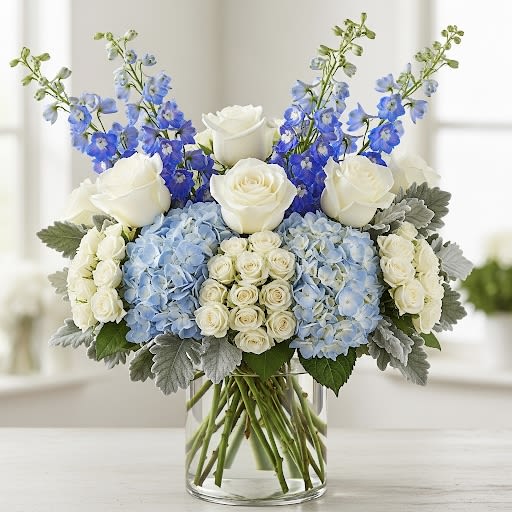 Ocean By Black Cat Florist Ocean By Black Cat Florist - Ocean — A serene tide of blooms flowing with grace. White roses and spray roses gleam like seafoam, while blue hydrangeas and delphiniums mirror the depth of open waters. Dusty miller drifts through with a silvery touch, evoking waves kissed by moonlight. Arranged in a clear glass cylinder vase, Ocean captures the elegance of the sea in a poetic embrace.