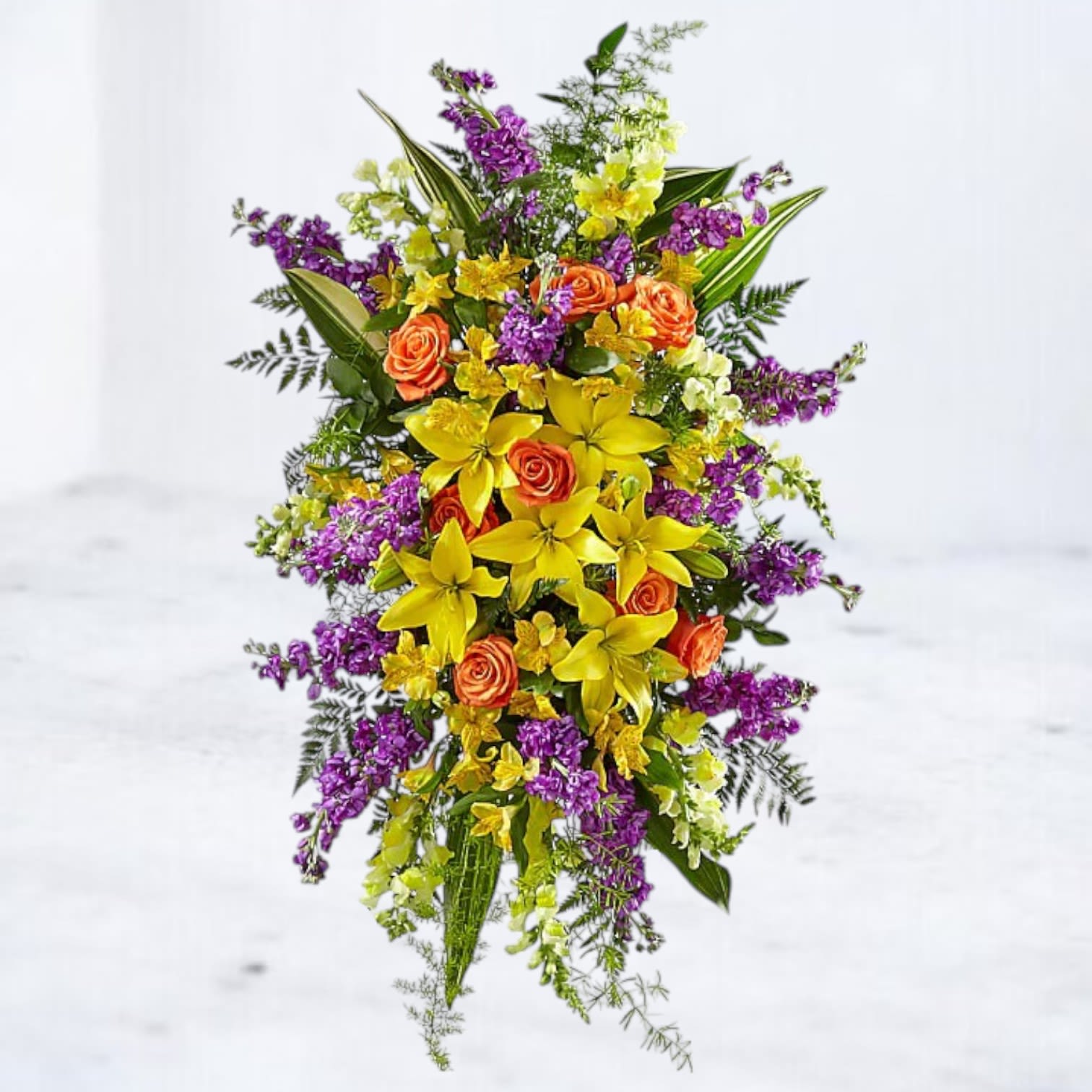 Golden Sunrise Standing Spray - Celebrate a vibrant life with the Golden Sunrise Standing Spray, a radiant funeral arrangement designed to convey hope, warmth, and love. Featuring an uplifting mix of bright yellow lilies, vivid orange roses, and soft purple stock, this standing spray creates a heartfelt tribute. Accentuated with lush greenery, it symbolizes renewal and remembrance, making it the perfect gesture of sympathy. Ideal for funeral services, this arrangement stands as a beautiful representation of a life well-lived.  Easels are included with all standing sprays for effortless display at services.