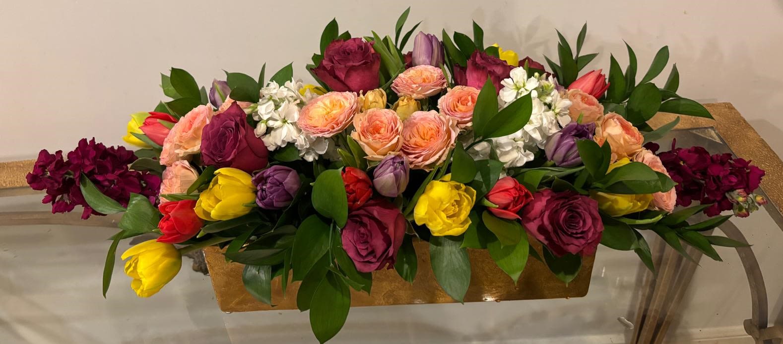 Garden Festival Garden Festival - A joyful and abundant arrangement bursting with color, featuring vibrant yellow, red, and purple tulips, peach garden roses, bold fuchsia roses, and delicate white blooms. Accented with lush greenery and presented in an elegant gold container, this lively design brings the energy and beauty of a spring garden to any celebration or special occasion