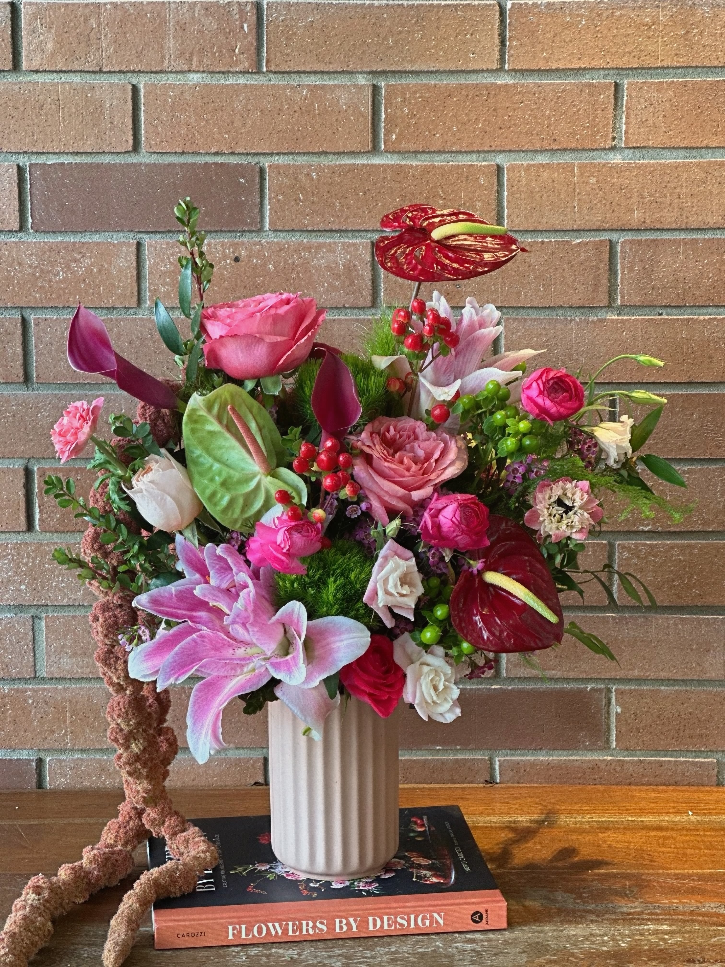 Summer Dance Tropical Bouquet  - At Venetian Flowers, we hand create our fresh bouquets with the best quality flowers, and this stunning arrangement perfectly captures the magic where summer meets fall. Featuring vibrant pink and coral garden roses, exotic red anthuriums, fragrant Oriental rose-lilies, and rich burgundy calla lilies, this design celebrates the season’s transition with its bold palette of magenta, coral, and deep wine tones. Accented with cheerful hypericum berries, delicate lisianthus, and textural greenery, each bloom is carefully selected and artfully arranged to create a sophisticated balance of warmth and elegance. Presented in a classic white ribbed vessel, this locally crafted arrangement brings the beauty of Venice’s unique seasonal charm to any space.”