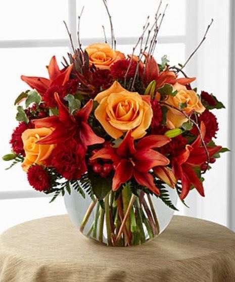 Autumn Harvest Bouquet - Bring the warmth of fall into your home with the &quot;Autumn Harvest Bouquet&quot;!  This stunning arrangement features vibrant orange roses, bold red lilies, and rich red carnations in a clear glass vase. Twigs add a natural touch, evoking the cozy feel of autumn. Perfect for decorating your table or gifting to loved ones for the fall season. 