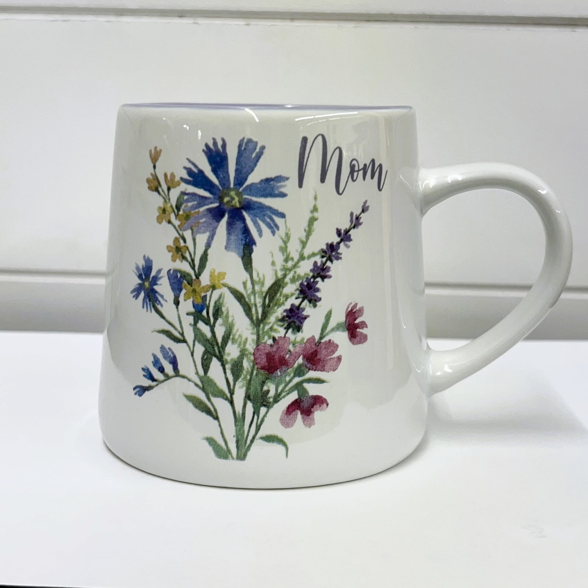 Mom Mug Floral - LOCAL DELIVERY AND PICK UP ONLY Mom Mug Floral - LOCAL DELIVERY AND PICK UP ONLY - Ceramic mug with a blue, yellow and pink bloom design on a white background. Has the message "Mom" on top of the bloom.